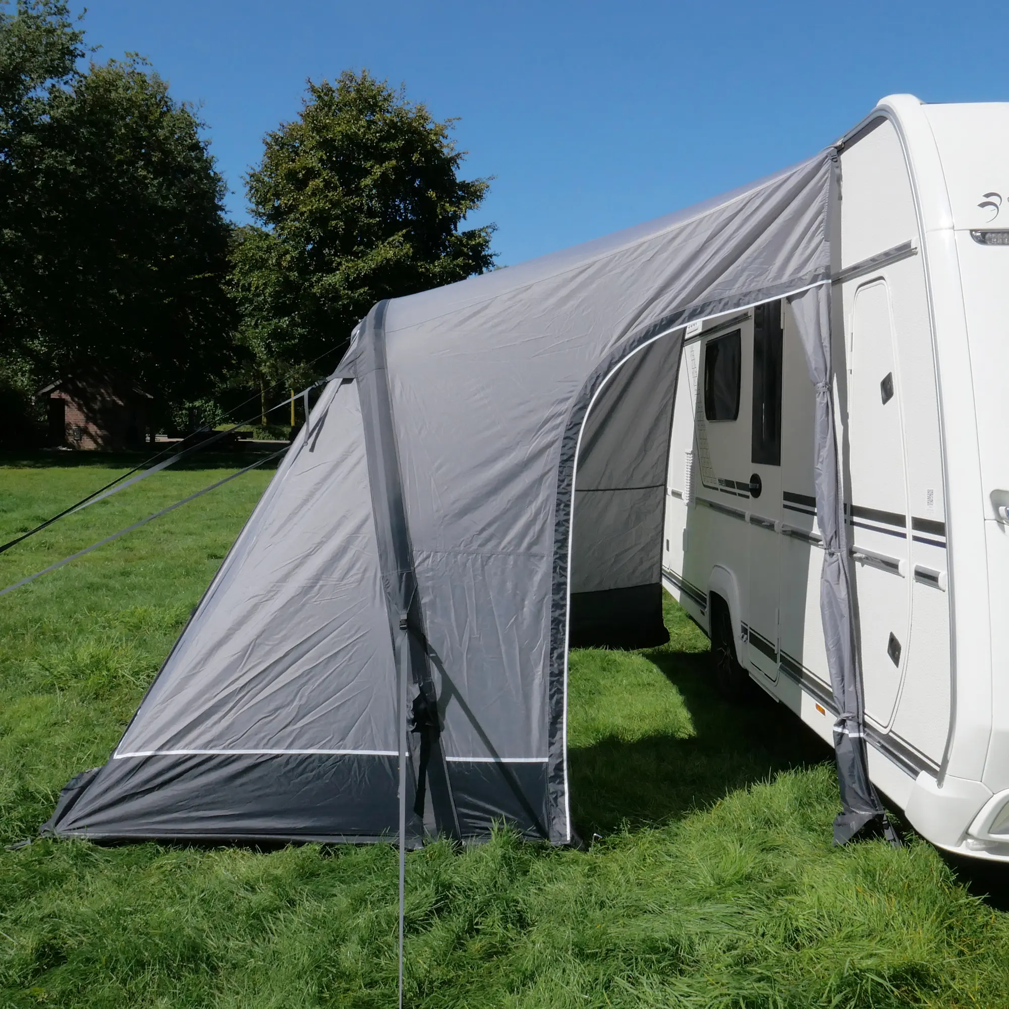 your GEAR Vicenza 350E AIR inflatable awning, 350 x 250 cm, attached to a caravan, lightweight gray fabric, single air tube frame, large entrance, set up on grass under clear blue sky.
