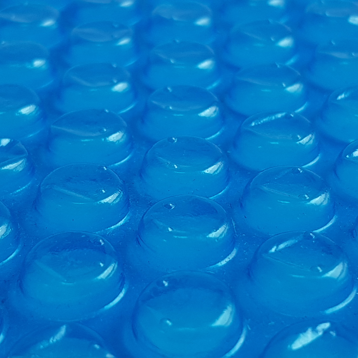 Close-up of your GEAR Solarplane SC-400x200 pool solar cover, showing the blue 300 µm thick bubble solar film surface designed for heating pool water with solar energy.