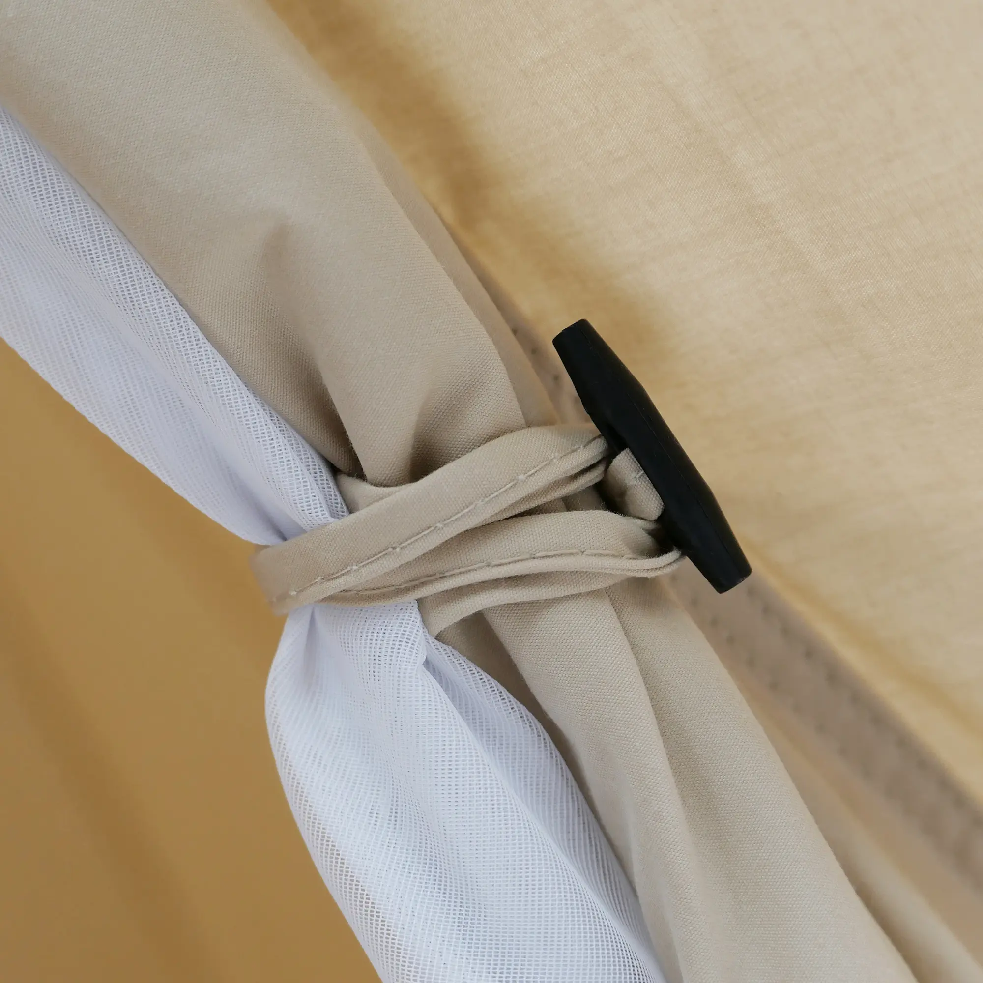Détail du yourGEAR Zelt Desert 8 Pro : tissu beige en coton-mix, moustiquaire blanche enroulée et fixée avec une lanière cousue et un bouton noir, montrant la qualité et la finition du tipi familial.