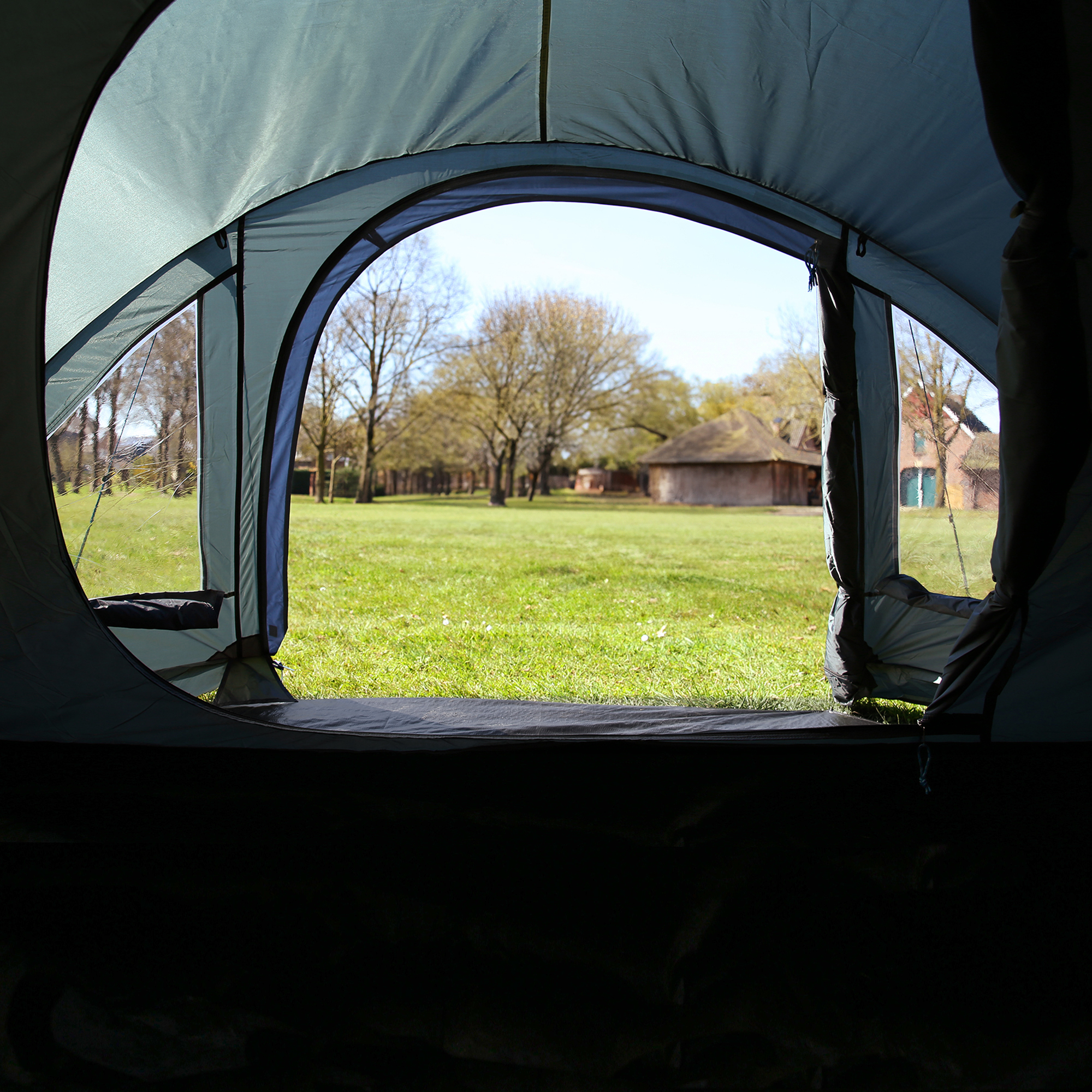 Vista desde el interior del your GEAR Zelt Monza, tienda de campaña tipo cúpula para 4 personas, con suelo y ventanas de PVC, mostrando su amplio vestíbulo y protección UV50+ en un entorno de camping.