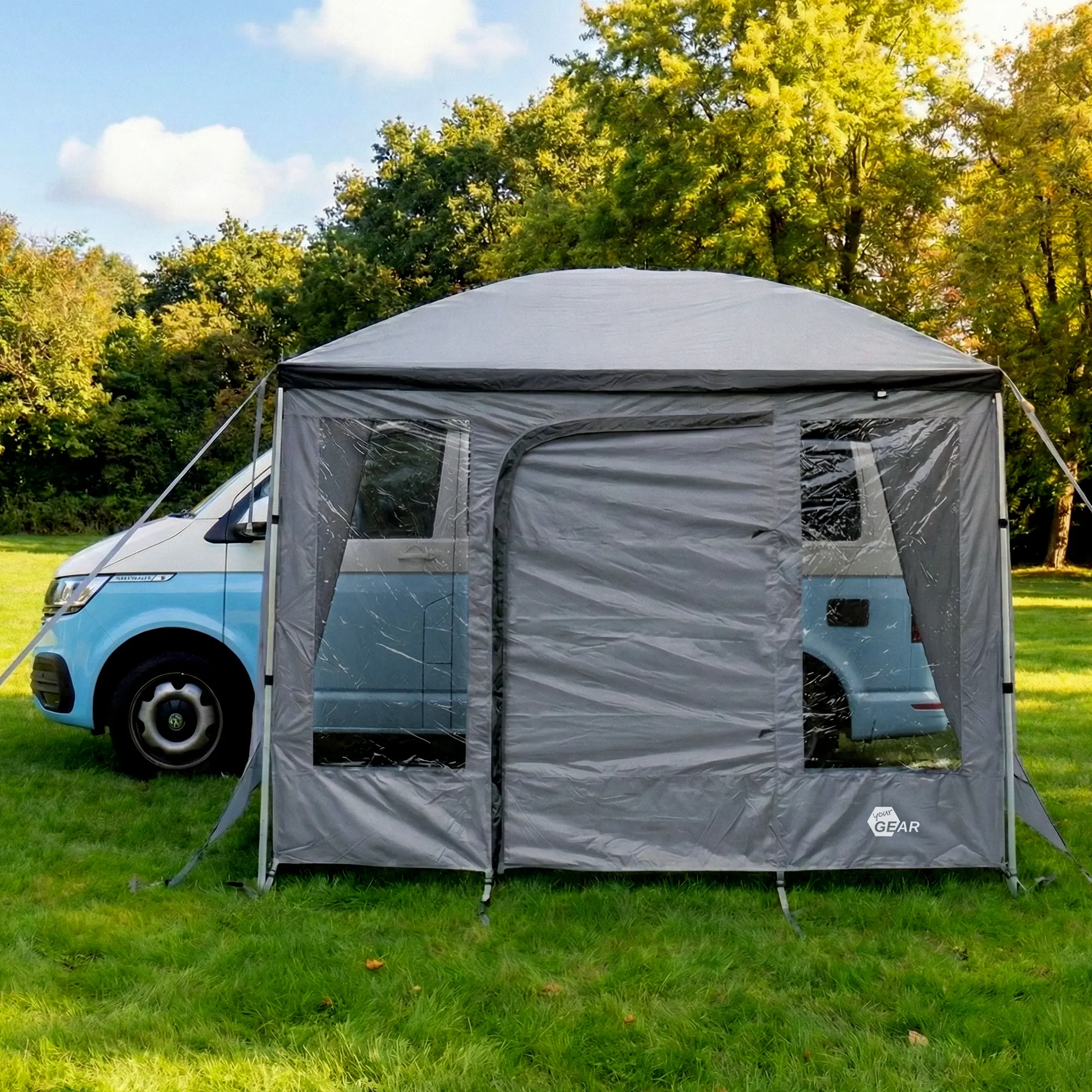 Frontale Ansicht der your GEAR Parasol Vorderwand 260x235 cm mit Tür und zwei Fenstern, wetterfest, UV 50+, 5000 mm Wassersäule, an einem Campingbus montiert, auf grüner Wiese im Freien.