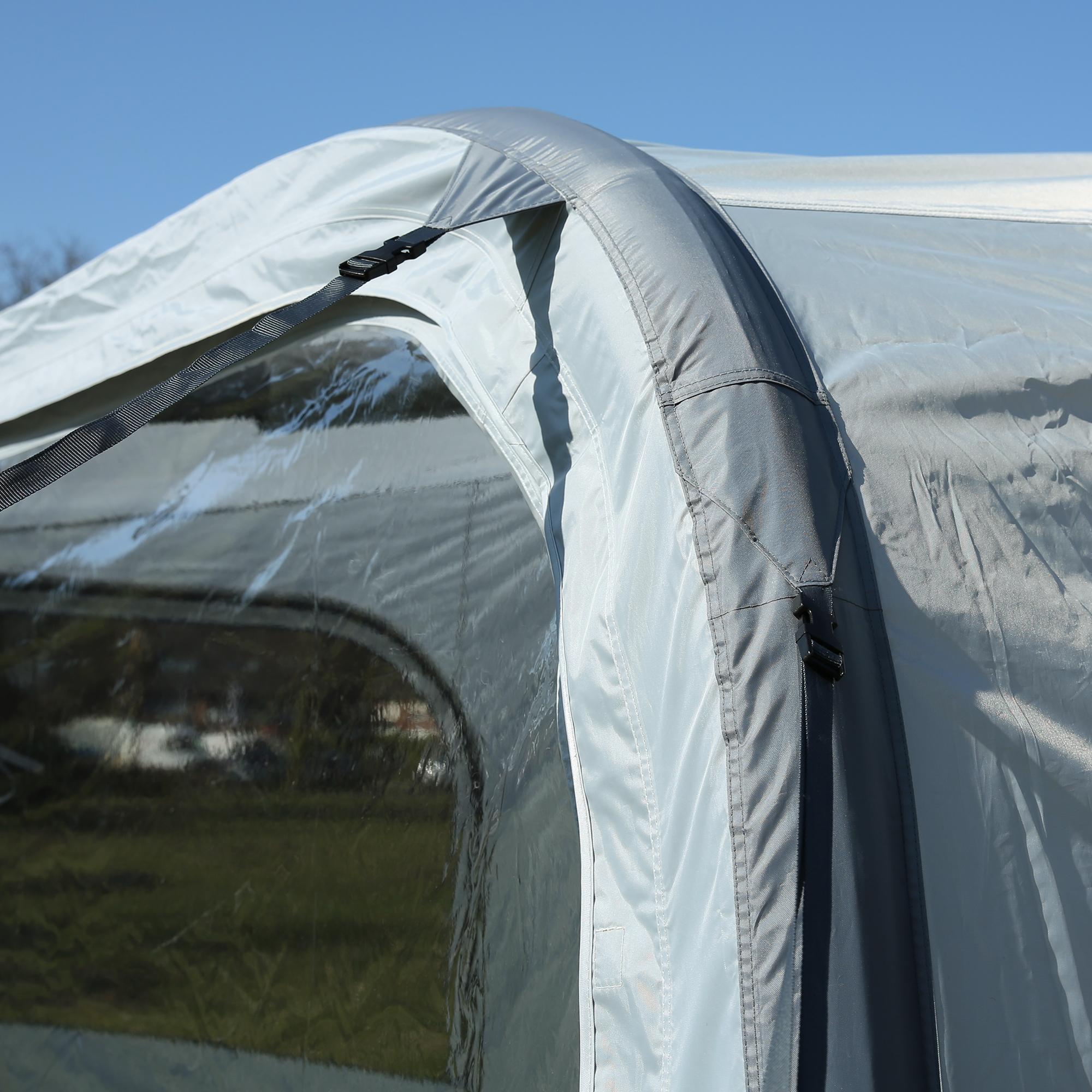 Dettaglio di una tenda da campeggio gonfiabile grigia con finestra trasparente, vista all’aperto sotto un cielo azzurro.