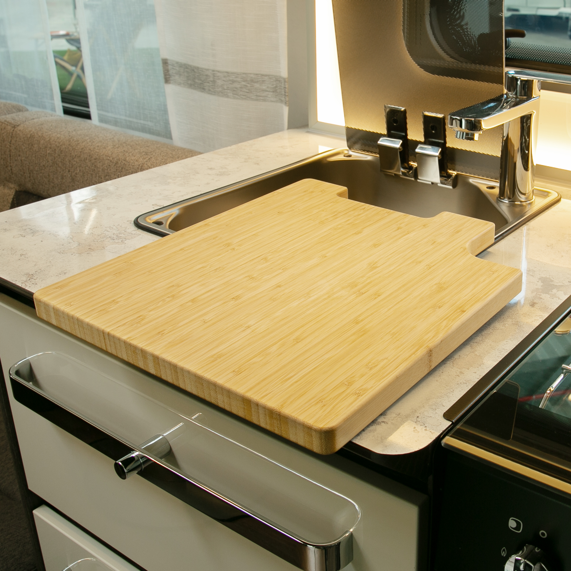 Planche à découper en bambou your GEAR Burano, utilisée comme couvercle d’évier dans une cuisine de camping-car, surface lisse, forme adaptée, augmente l’espace de travail, robinet visible à côté.