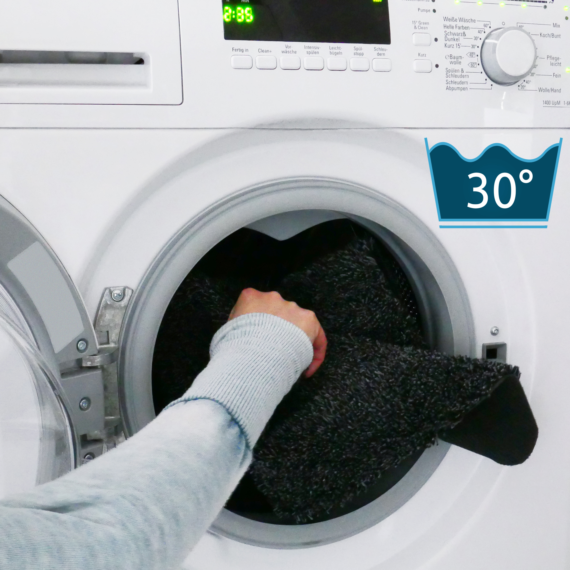 Hand placing a grey yourGEAR self-adhesive stair mat with TPR backing into a washing machine, showing the mat is machine washable at 30 degrees Celsius. Ideal for anti-slip stair protection.