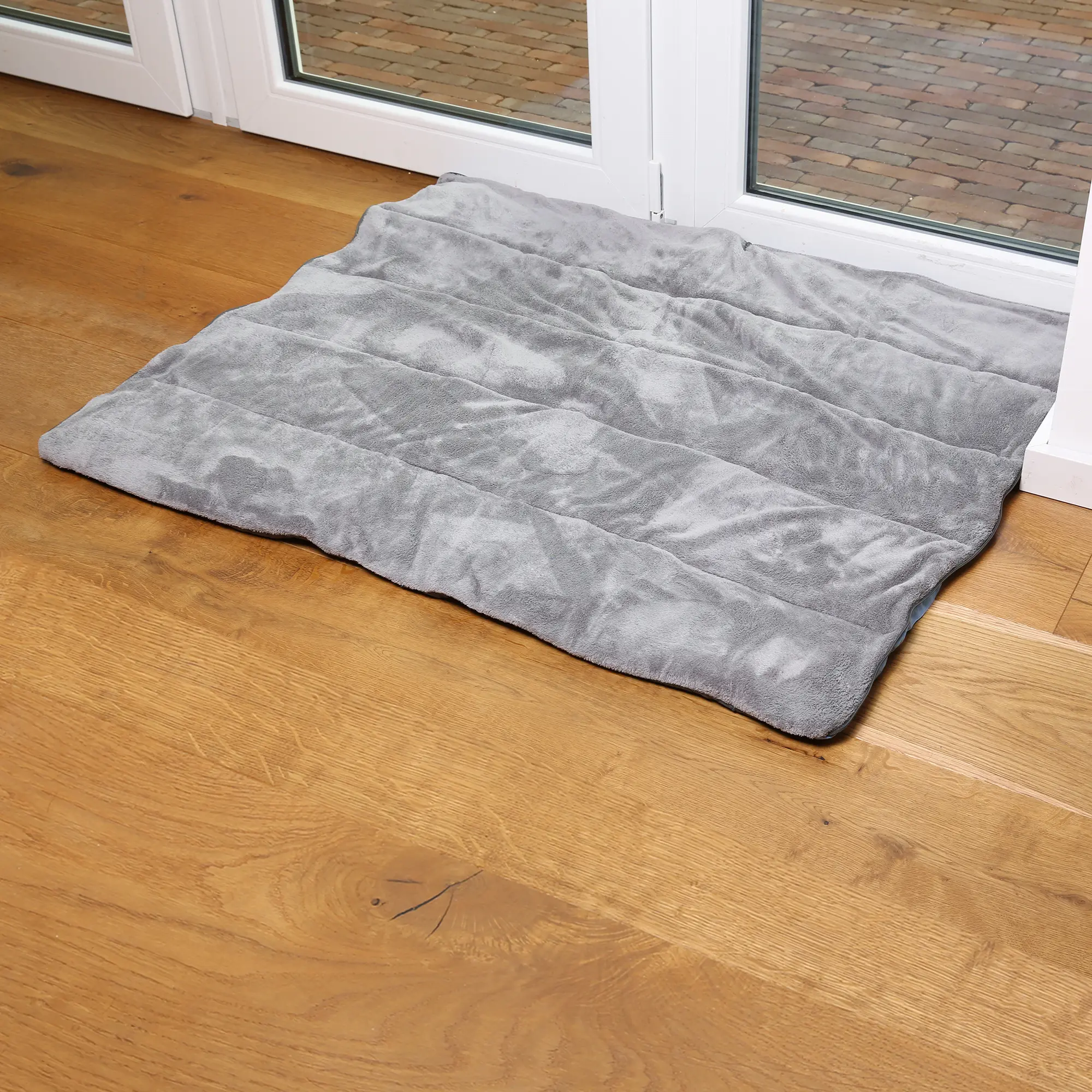 your GEAR Lodi 3-in-1 Hundeschlafsack, Hundedecke und Hundehandtuch in Grau, weich, gesteppt, rechteckig, auf hellem Holzboden vor einer Terrassentür, ideal für Reisen und Camping mit Hund.