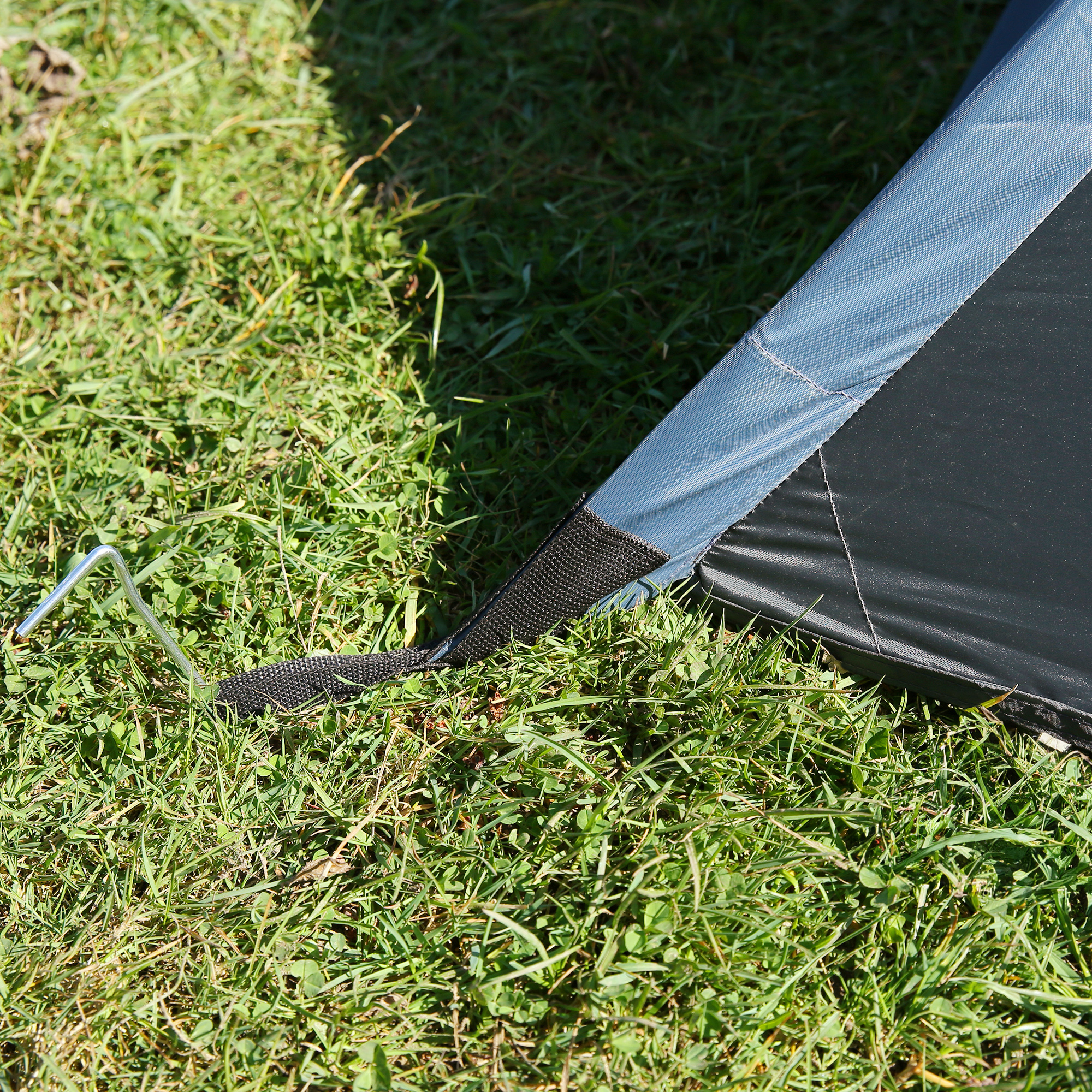Detalle de la esquina del your GEAR Zelt Monza para 4 personas, mostrando la lona resistente, costuras reforzadas y piqueta metálica anclada al césped para mayor estabilidad en camping.