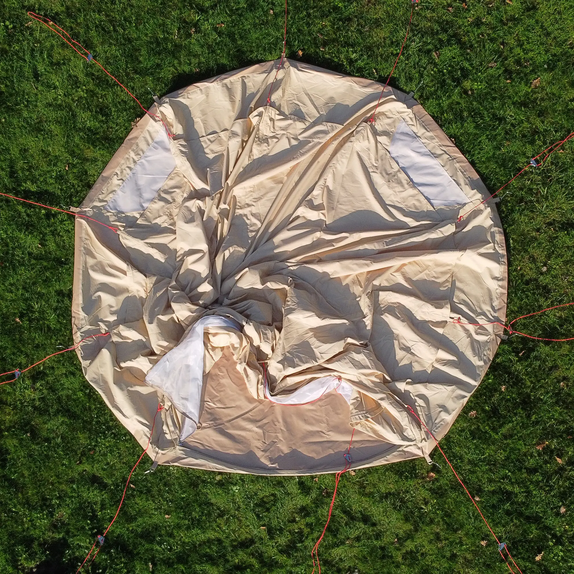 Top view of the your GEAR Gobi 3 tipi tent in beige cotton blend, laid flat on grass with red guy lines attached, showing mesh windows and entrance; UV50+ protection, no center pole, suitable for 2-3 people.
