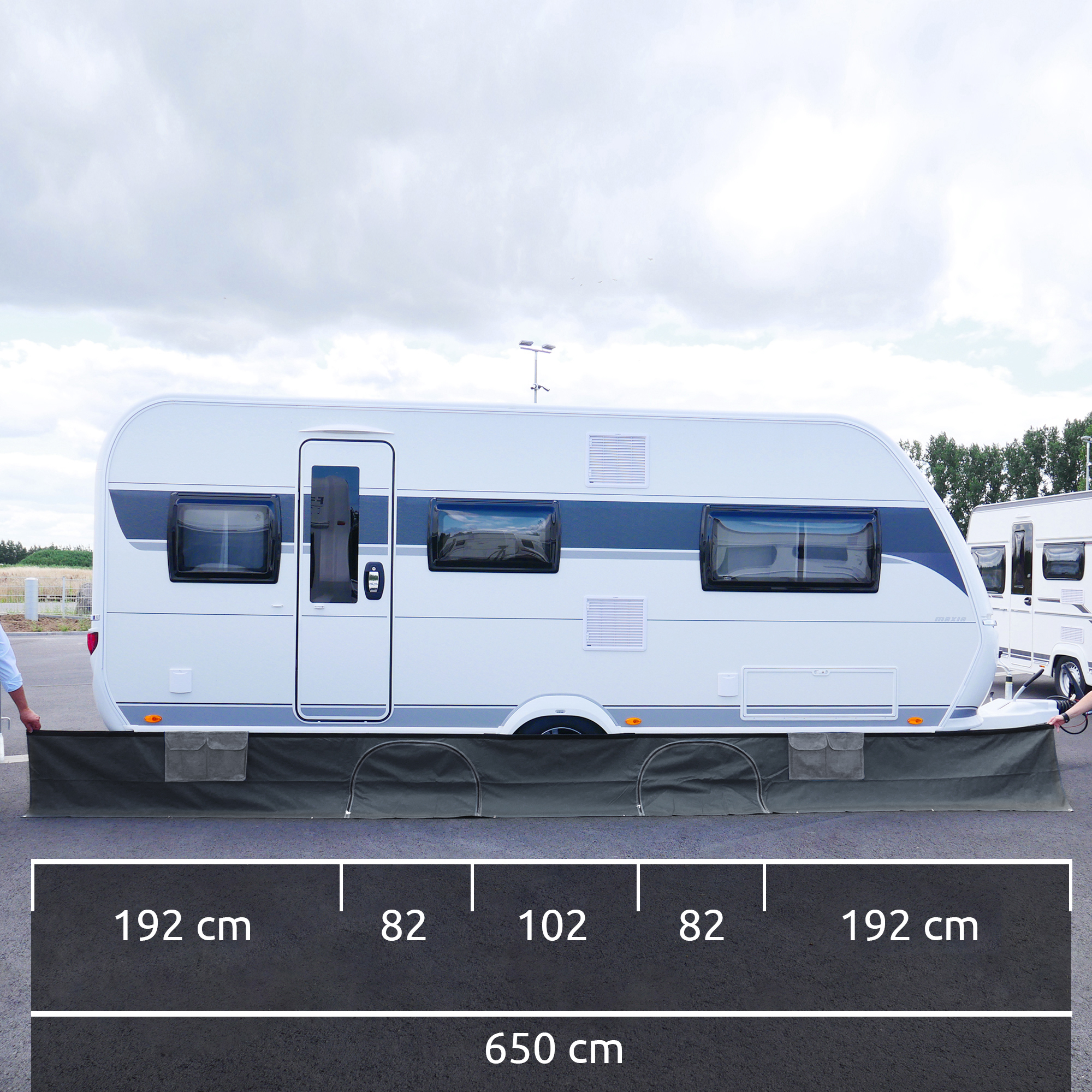 Wohnwagenschürze yourGEAR Draftskirt, 650 x 60 cm, schwarz, mit 2 Staufächern und Organizertaschen, vor einem Caravan montiert, Maße und Abschnitte der Schürze sind im Vordergrund eingezeichnet.