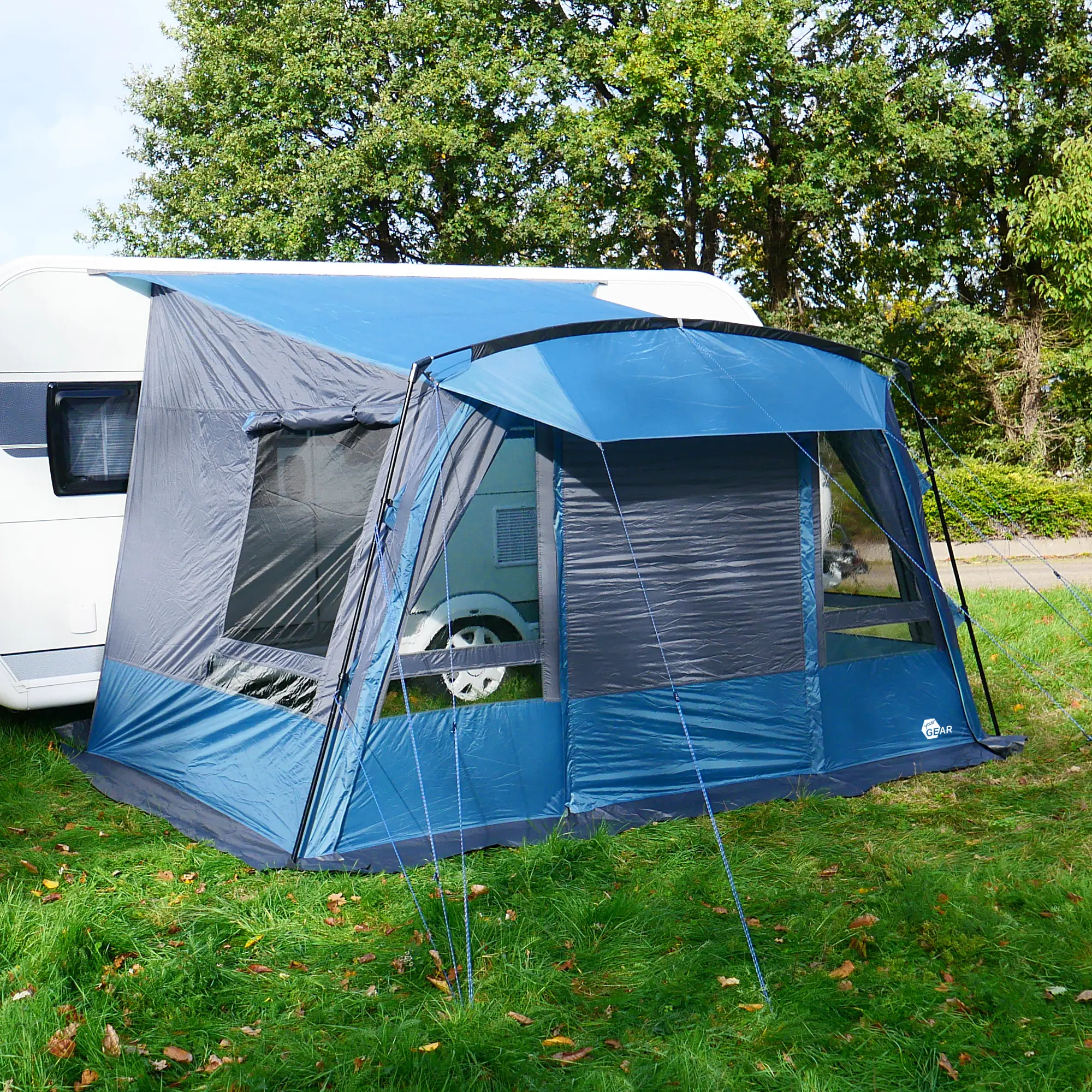Blau-graues your GEAR Malibu 350 Wohnwagenvorzelt mit großen Fenstern, herausnehmbarer Vorderwand und steilen Seitenwänden; aufgebaut an einem Caravan auf einer Wiese, ideal als Reisevorzelt.