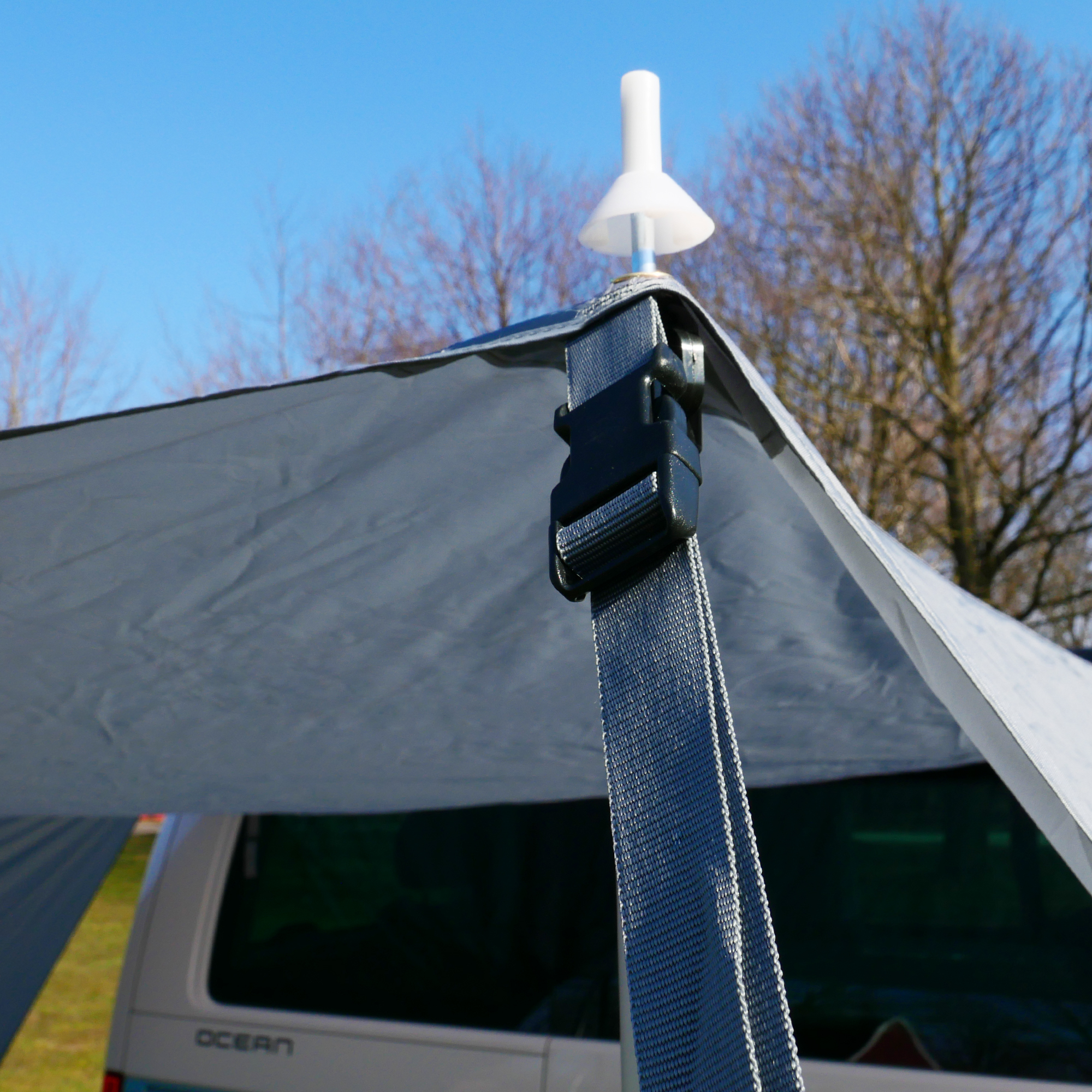 Close-up of your GEAR Tropea Bus awning UV 50+ with grey tarp, visible side wall, sturdy strap with buckle, and aluminum telescopic pole, mounted on a camper van for sun and rain protection.