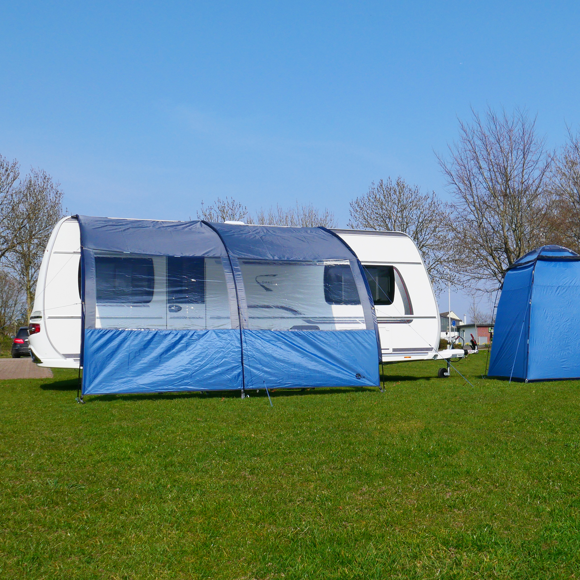 Auvent your GEAR Riviera 350 bleu avec grandes fenêtres panoramiques, installé devant une caravane, offrant protection solaire UV 50+ et abri contre la pluie, idéal pour camping et caravaning.