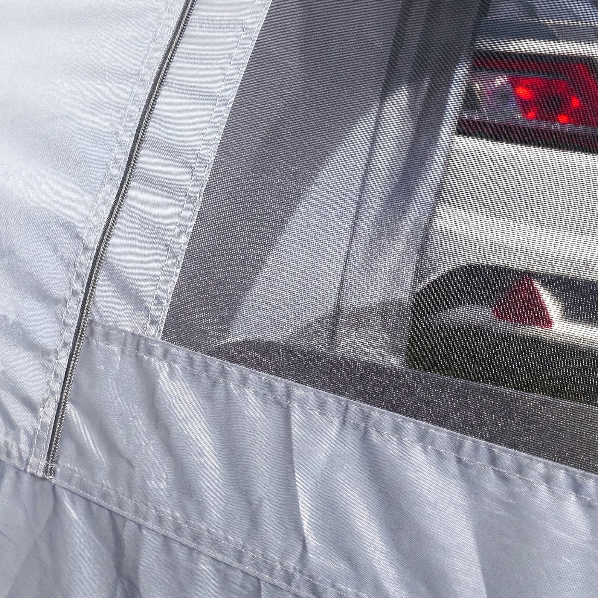Détail d'un auvent caravane your GEAR Venecia gris avec tissu imperméable, couture renforcée, fermeture éclair et panneau moustiquaire transparent laissant voir le feu arrière d'une caravane.