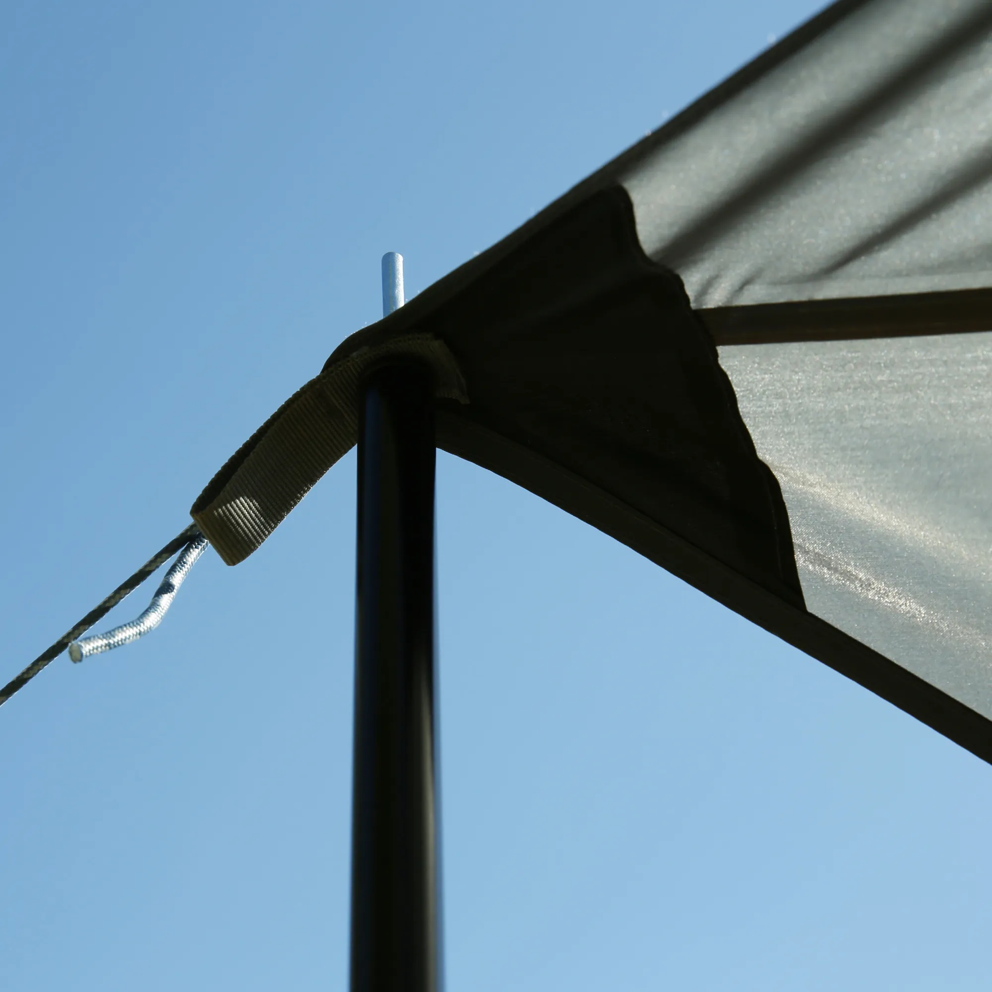 Close-up of grey your GEAR Atrani 3x3m sunshade tarp corner showing beige strap, black support pole and metal top pin against clear blue sky, waterproof fabric and reinforced edge visible.