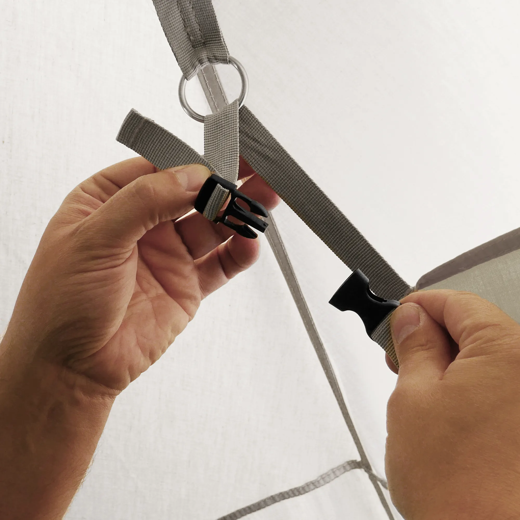 Close-up of beige Sonora PES sidewall attachment showing sewn fabric loop, metal O-ring, adjustable grey webbing straps and black plastic quick-release buckle held by hands for Sonora star tent pavilion.
