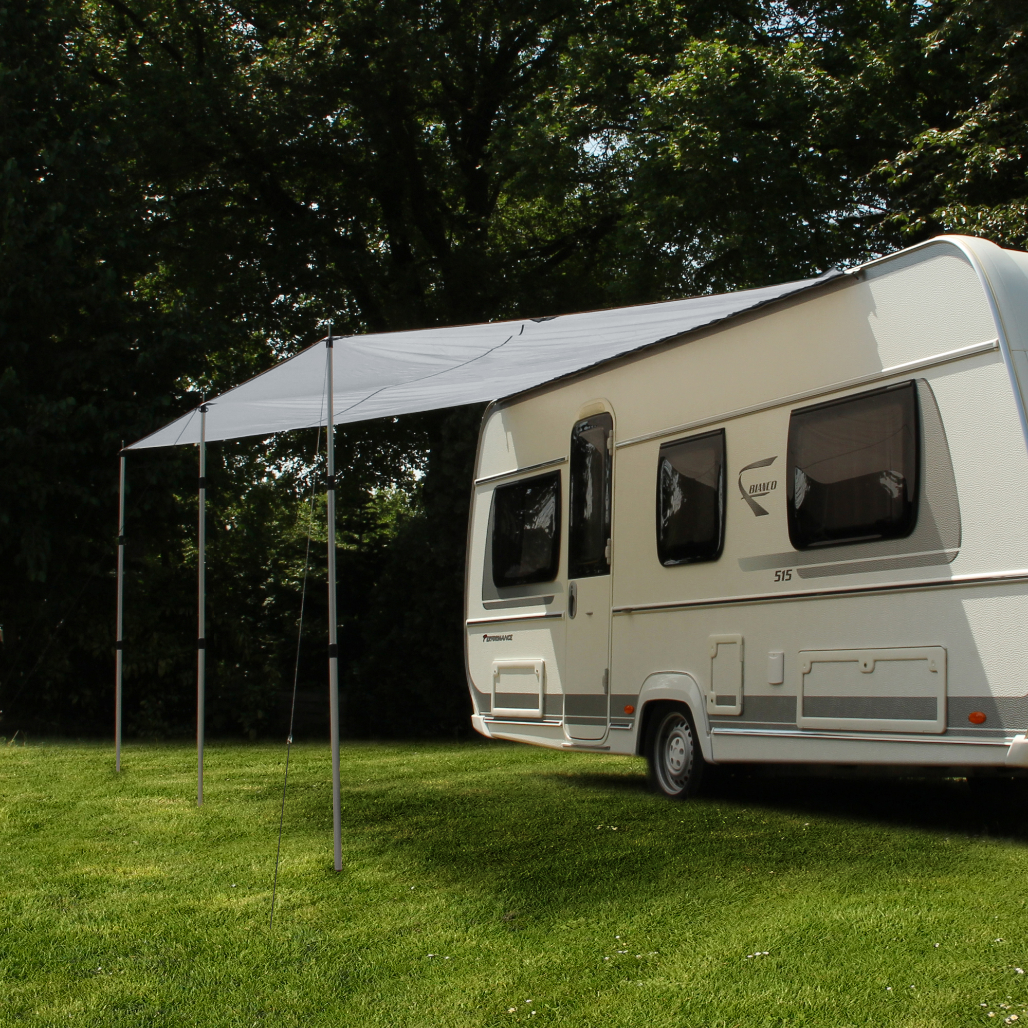 Toldo para caravana yourGEAR 3 x 2,4 m en gris, instalado con tres postes telescópicos de aluminio, proporciona sombra y protección UV 50+ junto a una caravana en un entorno verde.