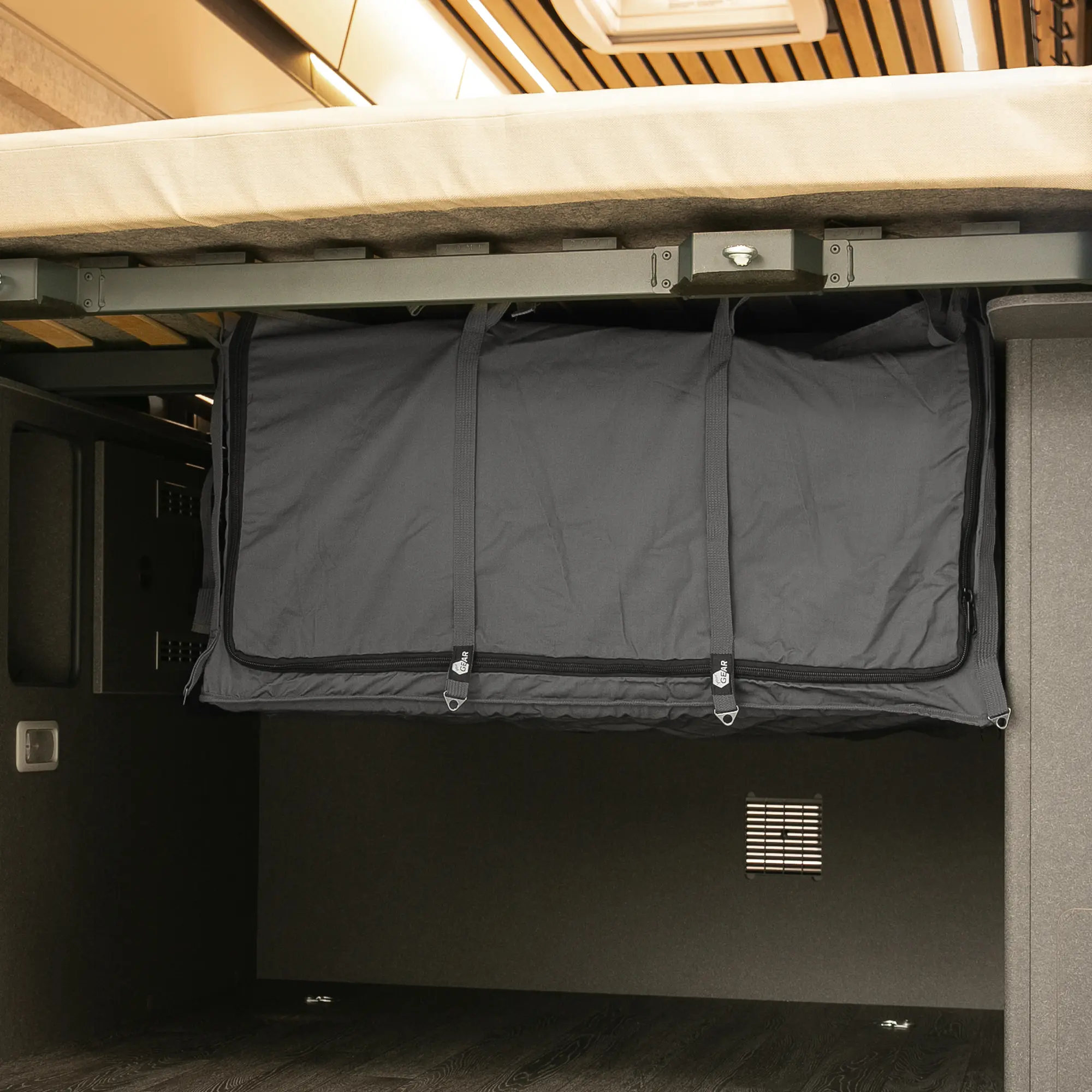 Sac de rangement your GEAR Catania noir, fixé sous le lit d’un van, offrant une solution d’organisation pratique pour la soute arrière, avec fermetures éclair visibles et design robuste pour accessoires de camping.