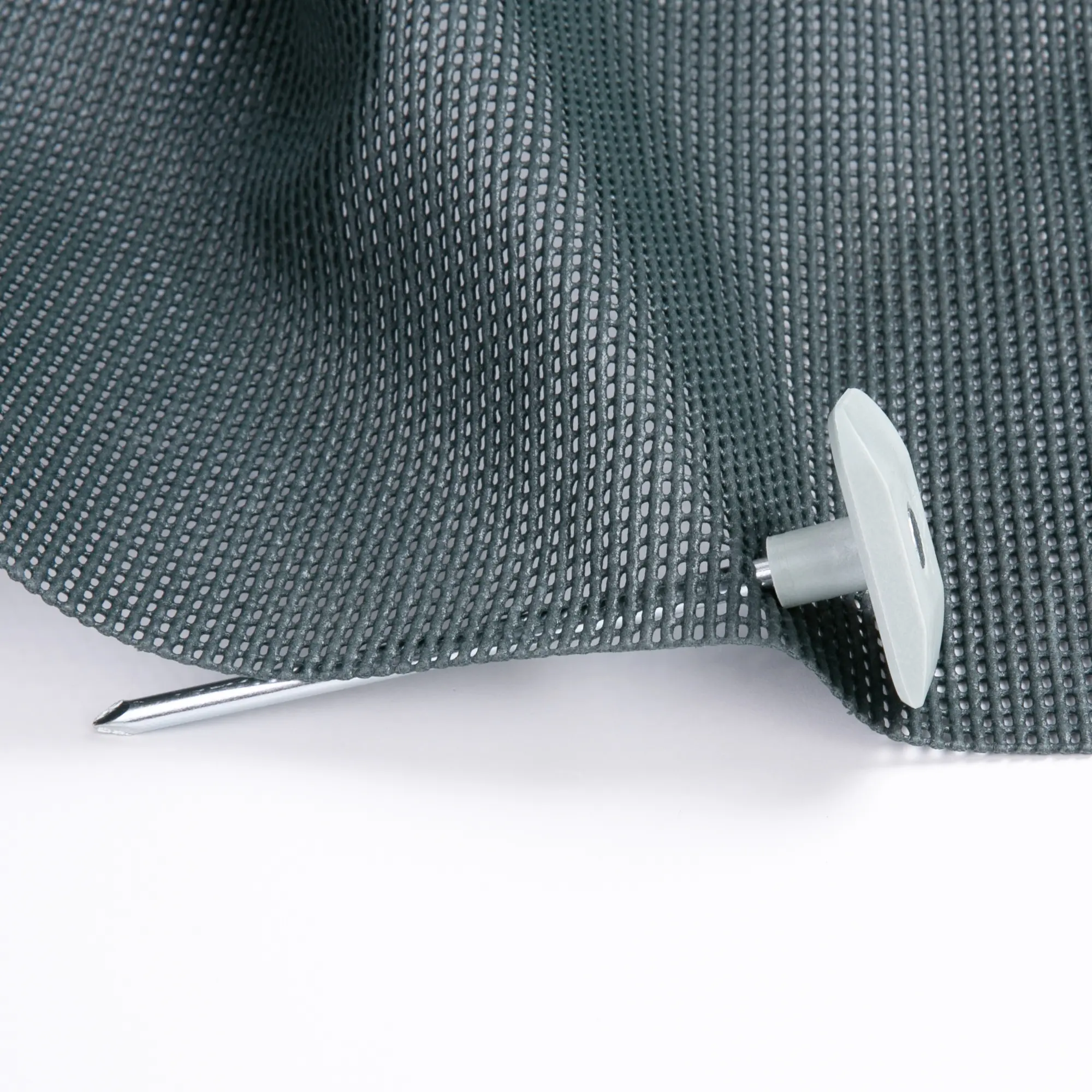 Hering your GEAR Safety Peg en acier avec tête plate en ABS, fixé dans un tapis de sol de tente gris à mailles, conçu pour éviter les chutes et sécuriser les tapis de camping ou auvent.