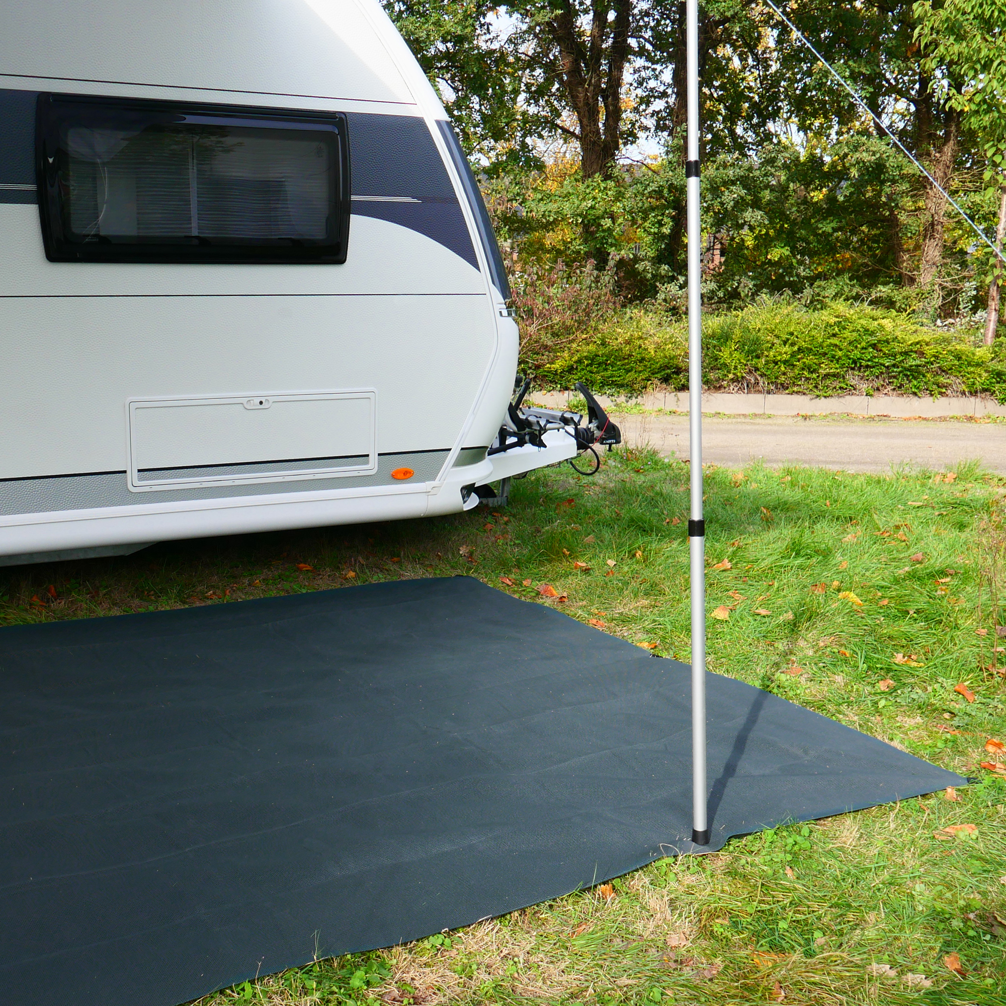 Tapis de sol extérieur your GEAR 300 x 400 cm, posé devant une caravane sur l’herbe, structure souple et perméable, idéal pour auvent ou camping, couleur gris foncé, résistant et facile à nettoyer.