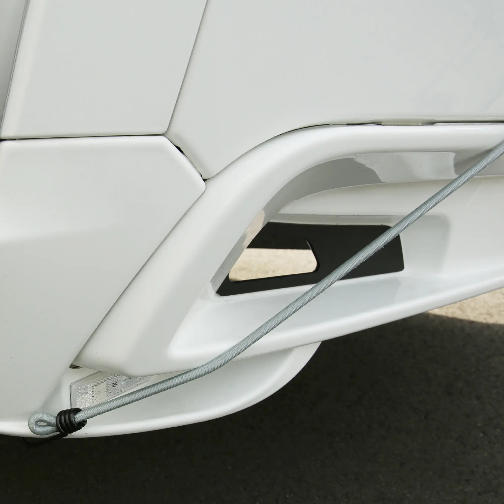 Detailansicht der your GEAR Caravan Bugschutzplane Thermo, zeigt eine gespannte, graue Befestigungsschnur an der weißen Karosserie eines Wohnwagens. Ideal als Front- und Heckschutzplane.