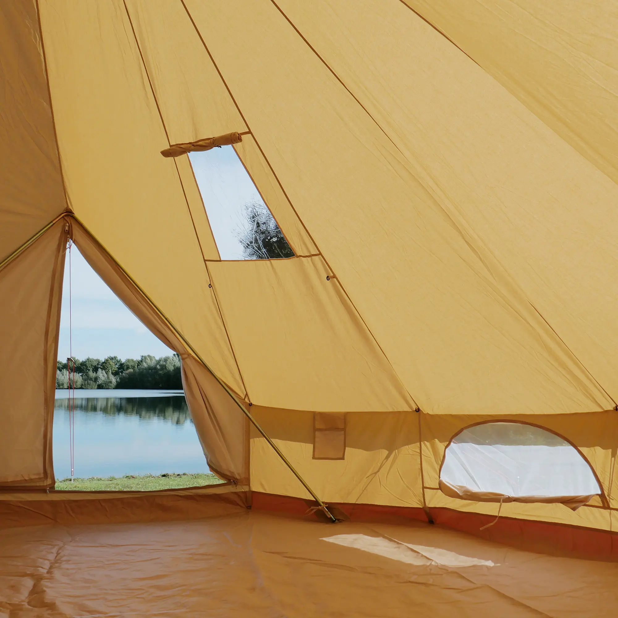 Intérieur du your GEAR Zelt Desert 8 Pro, grand tipi familial en coton, sol cousu en forme de baignoire, fenêtres avec moustiquaire et vue sur un lac, adapté pour 4 à 8 personnes, couleur sable.