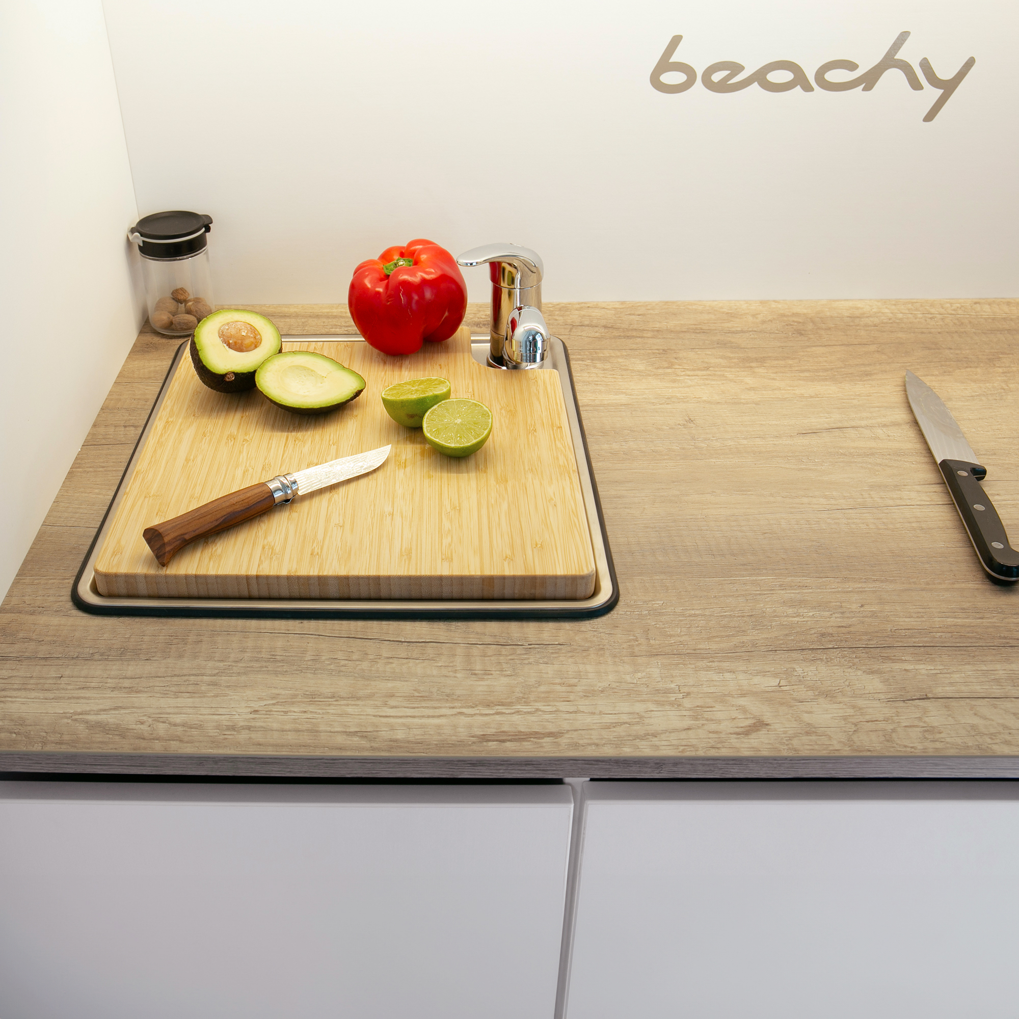 Planche à découper en bambou your GEAR Burano, posée sur un évier dans une cuisine de caravane, avec avocat, citron vert, poivron rouge et couteau, idéale comme couvre-évier et surface de travail.