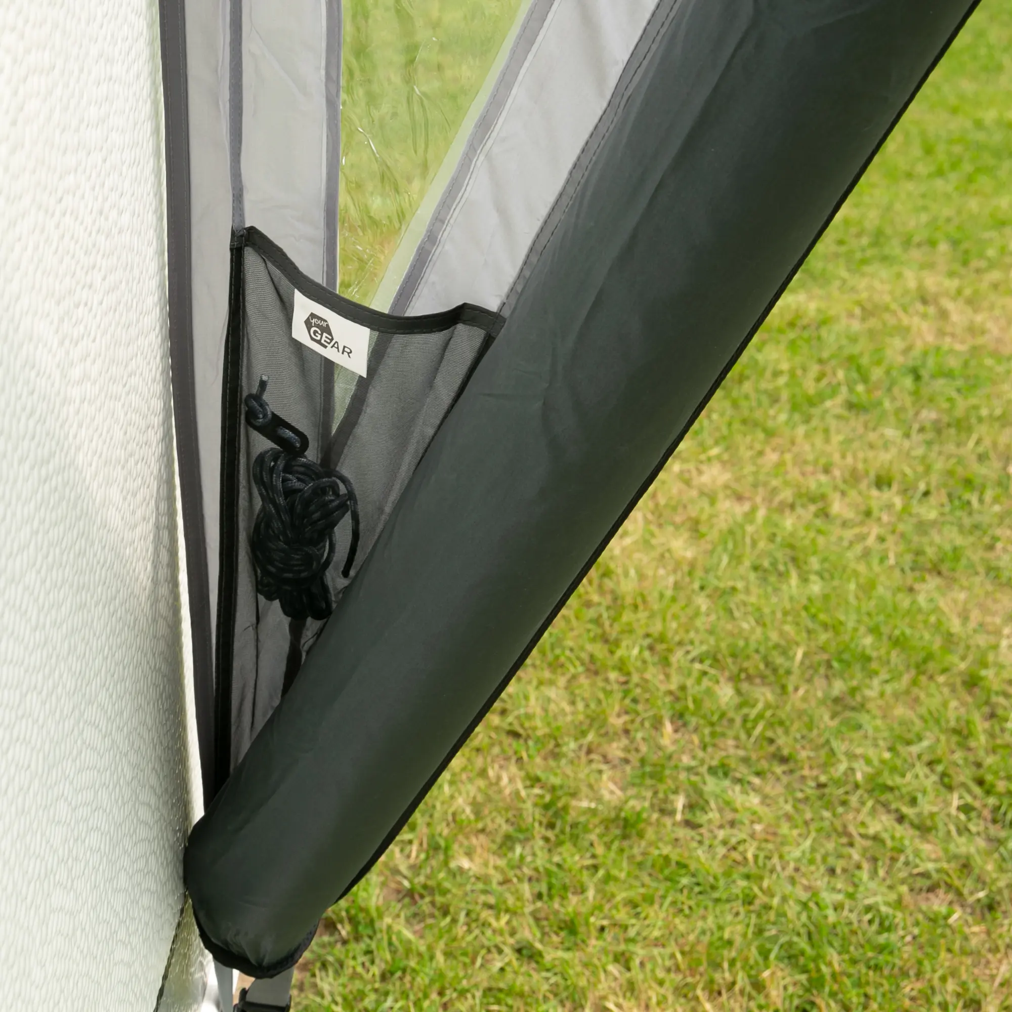 Detailaufnahme des your GEAR Tarent 180 Air Vordachs am Wohnmobil, mit aufblasbarem Gestänge, Seitentasche und sichtbarem Zubehör, aufgebaut auf grünem Rasen. Wetterschutz und Belüftung erkennbar.