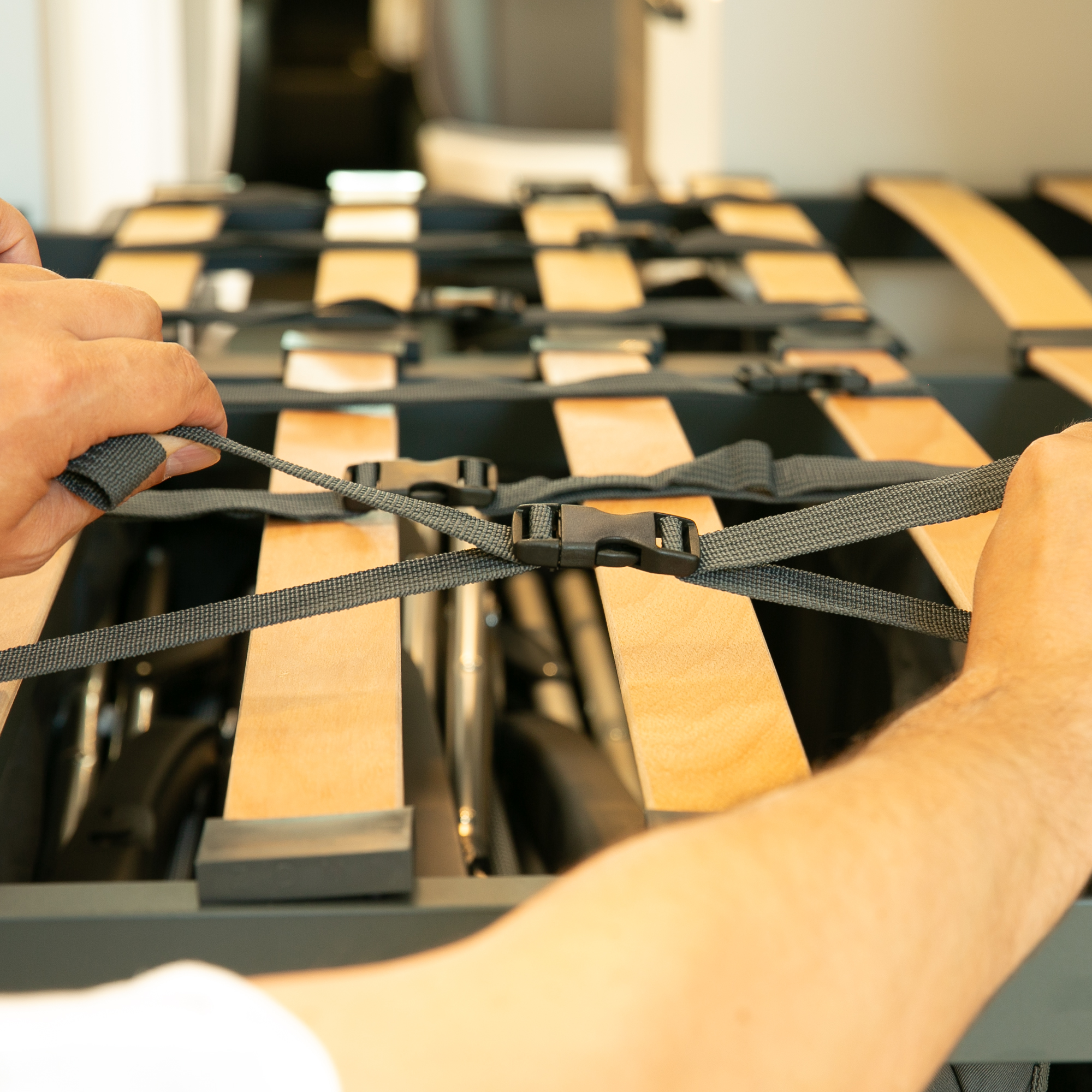 Close-up of a your GEAR Bozen storage bag in a camper van garage, showing hands securing adjustable straps over wooden slats to organize and secure camping furniture. Ideal for van storage and transport safety.