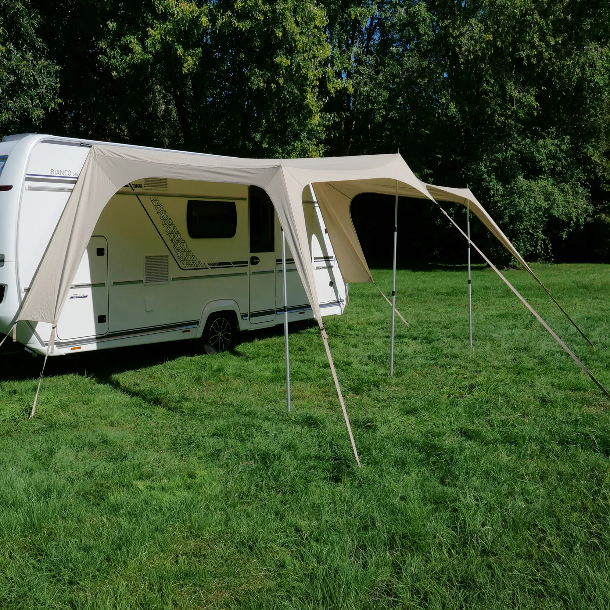 Beiges your GEAR Scilla TC Caravan Tarp 400x250 cm als Sonnensegel am Wohnwagen montiert, gespannt mit Stangen und Abspannseilen, auf einer grünen Wiese, bietet Schatten und Wetterschutz.