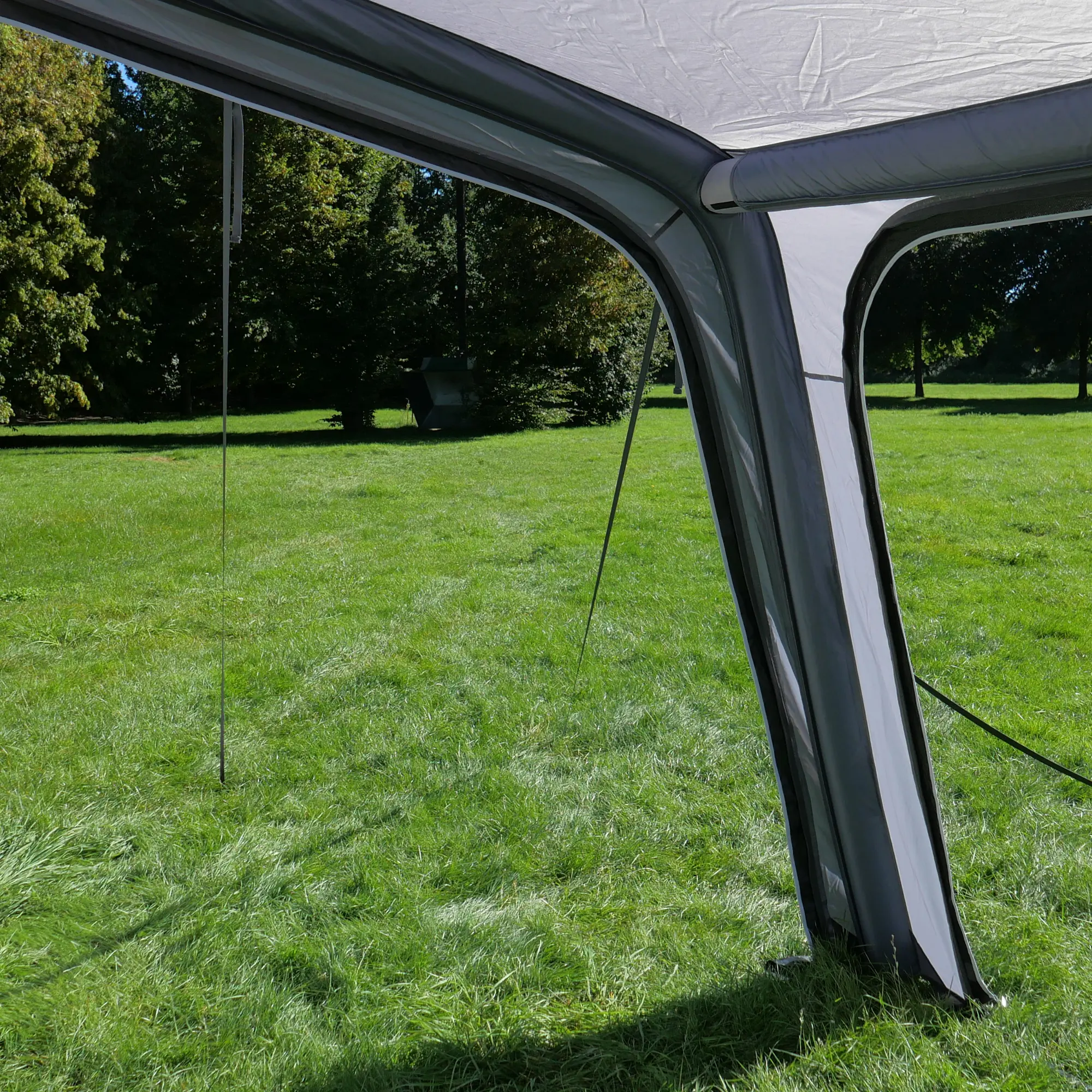 Avance de un toldo inflable your GEAR Porto 340 Air para caravana o autocaravana, estructura de tubos de aire y lona gris, instalado en césped, ideal como protección solar y contra la lluvia.
