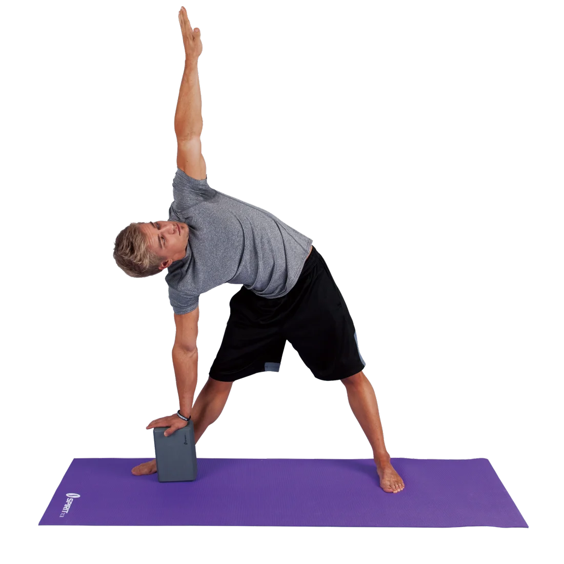Man performing yoga on a purple mat using a Spirit Yoga Block, 23x15x10 cm grey foam block, for support in a side stretch pose. The block provides stability and balance during the exercise.