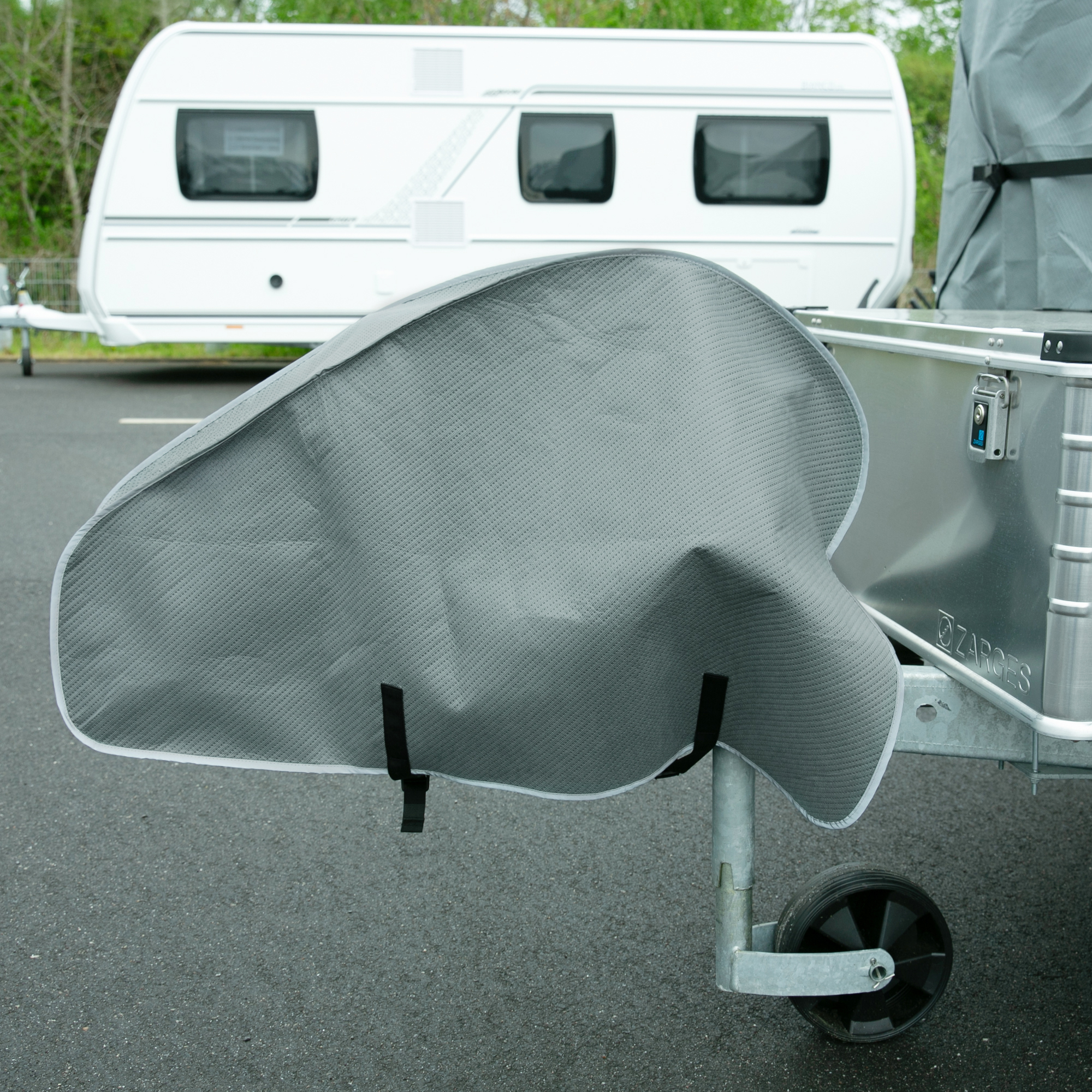 Grey your GEAR Bonito 430 - 470 caravan cover with included drawbar cover, made from four-layer polypropylene material, fitted securely on a trailer; caravan in the background. Weather protection product.