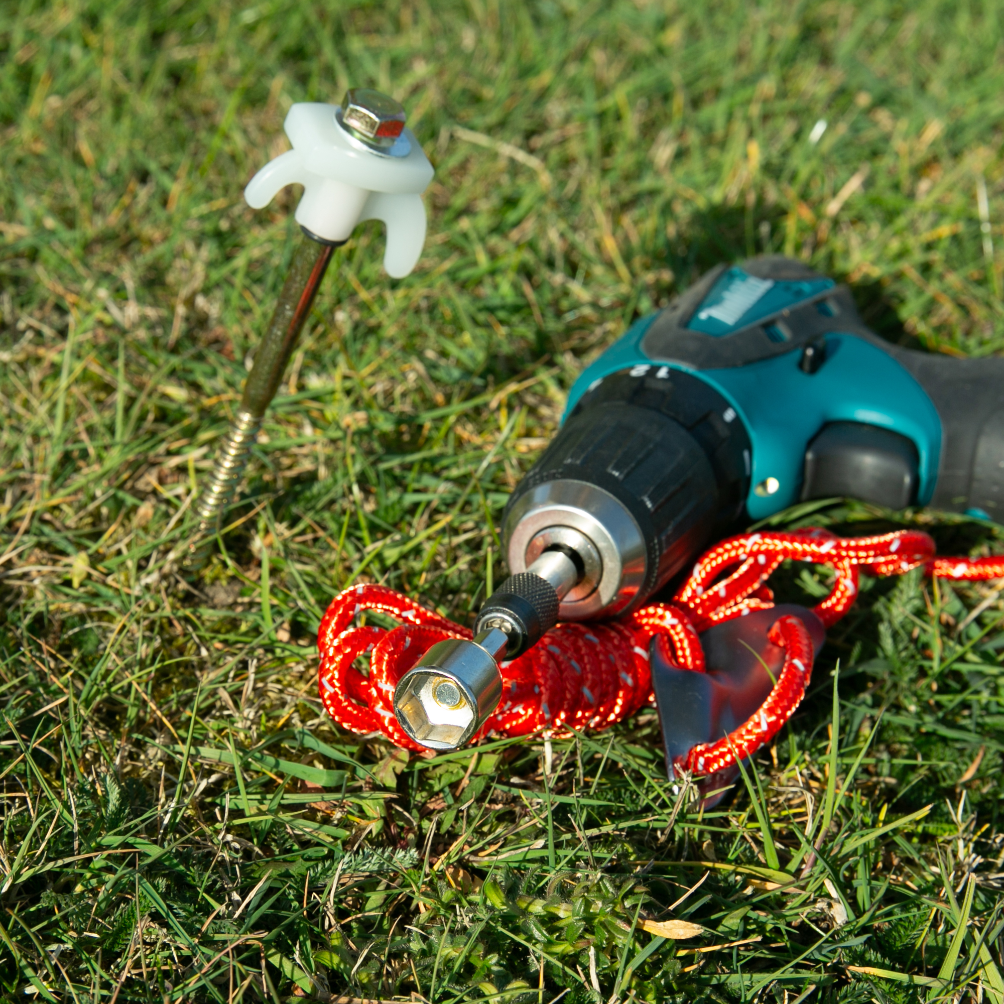 Robuster your GEAR Screw 200 Zelthering aus Stahl mit Sechskantkopf, fluoreszierendem Kunststoffkopf und Haken, daneben Akkuschrauber mit 13 mm Bit und roter Abspannleine auf Gras. Ideal für Camping.