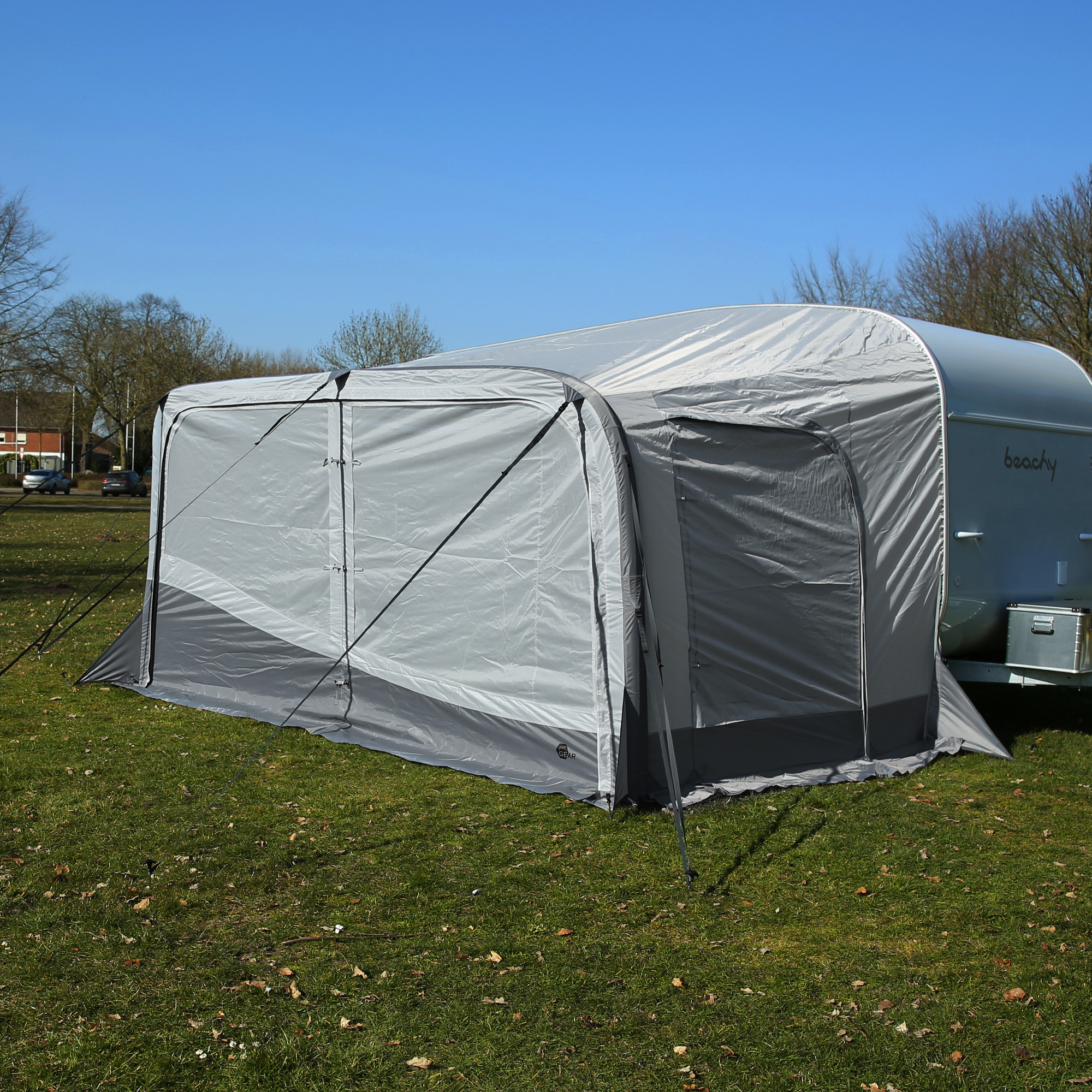 Tenda grigia da campeggio montata accanto a una roulotte su un prato verde sotto un cielo sereno.