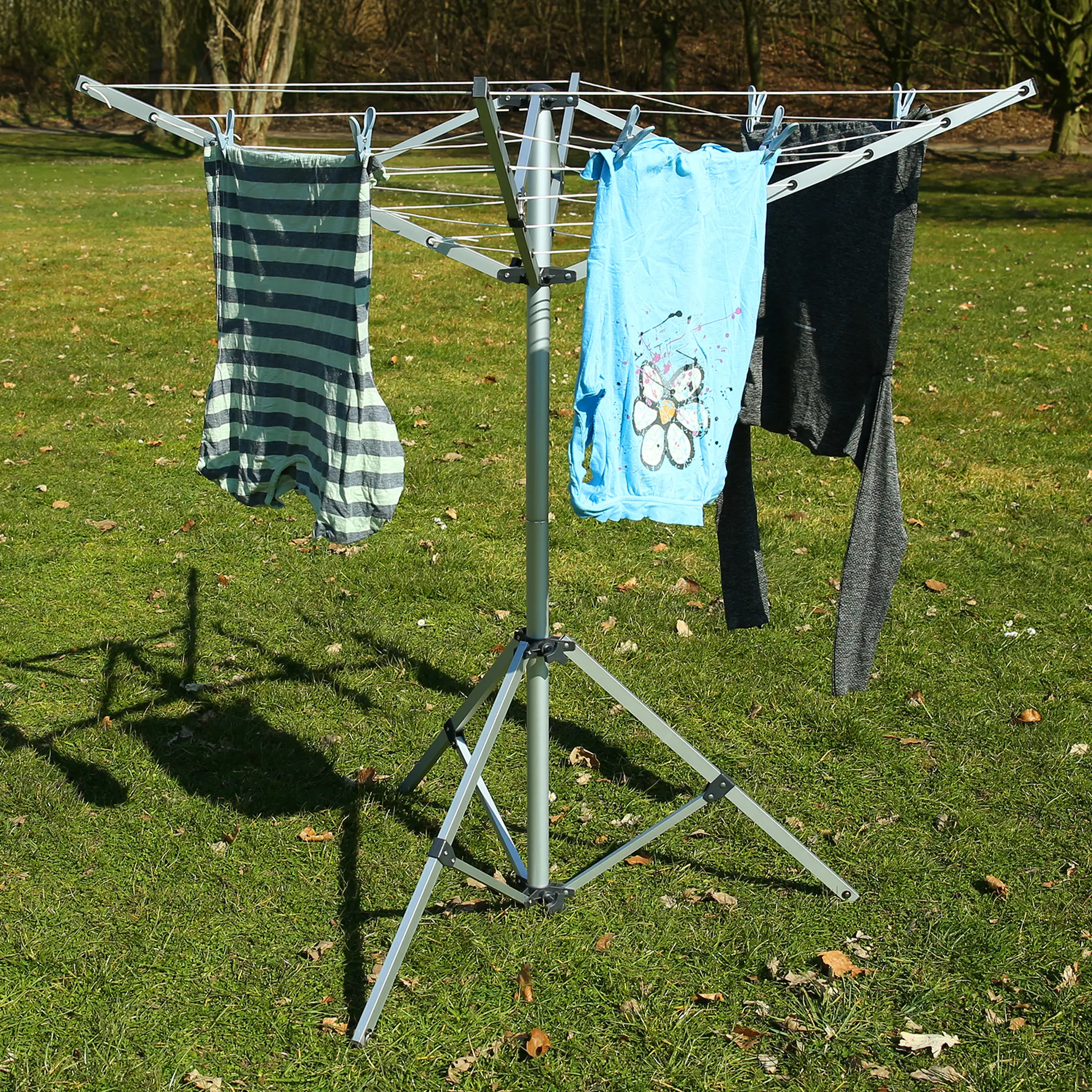 Wäschespinne your GEAR Siena aus Aluminium mit vier Armen und Standfuß, auf einer Wiese aufgestellt, bestückt mit aufgehängter Kleidung, ideal für Caravan und Camping.