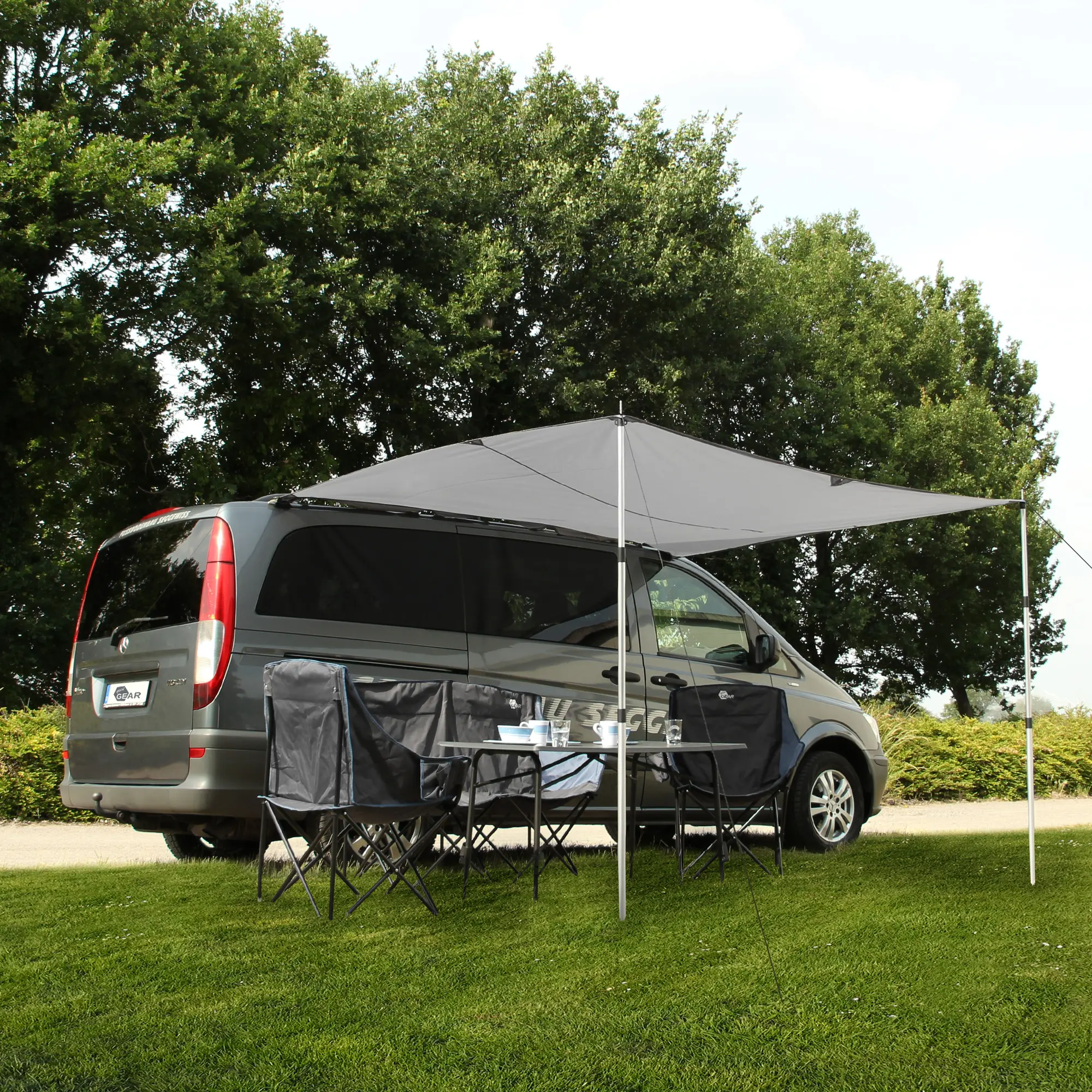 yourGEAR Motorhome Tarp 260 x 240 cm sun canopy in cool grey, mounted on a camper van with two aluminum poles, providing UV 50+ and rain protection. Outdoor chairs and table set up underneath.