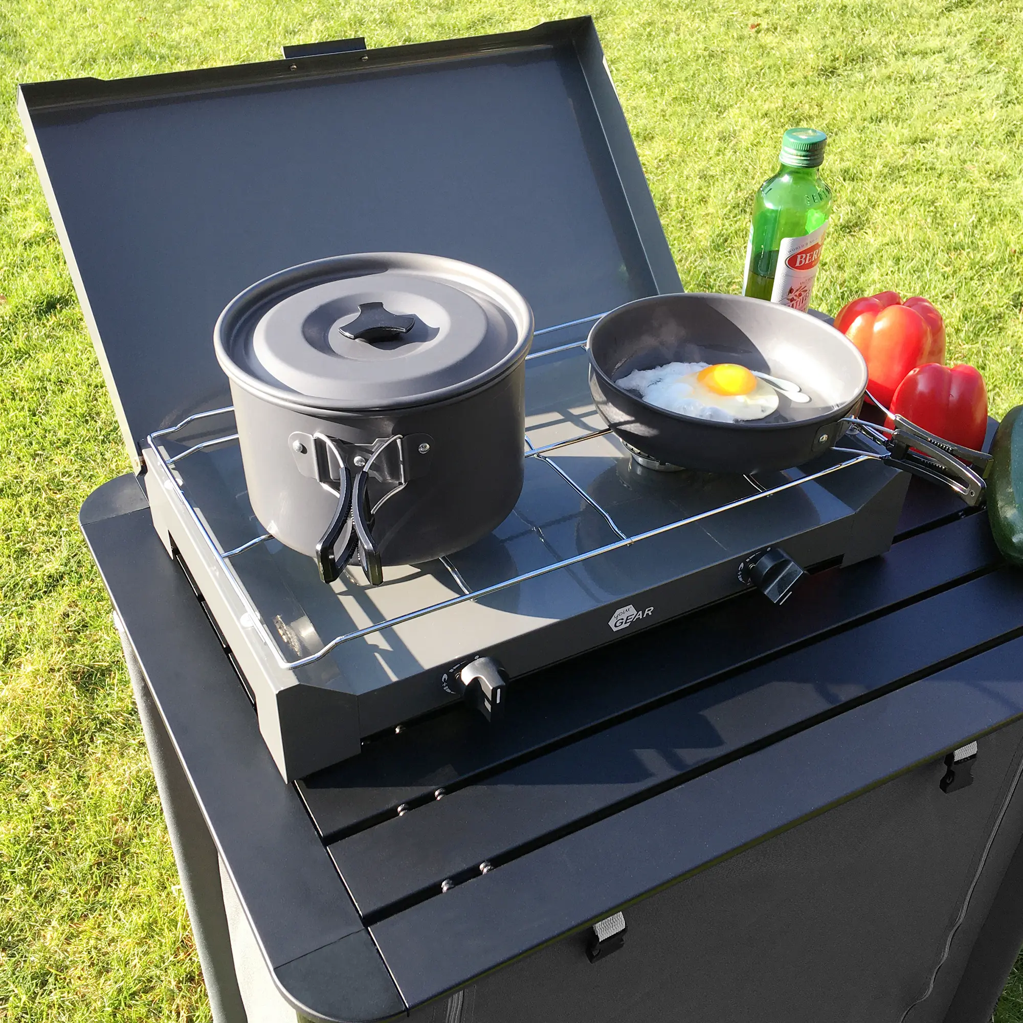 your GEAR Ranger V 7-piece camping cookware set with pot and frying pan for 4-5 people, shown on an outdoor stove; pot with lid and pan with fried egg, vegetables and oil bottle in background.