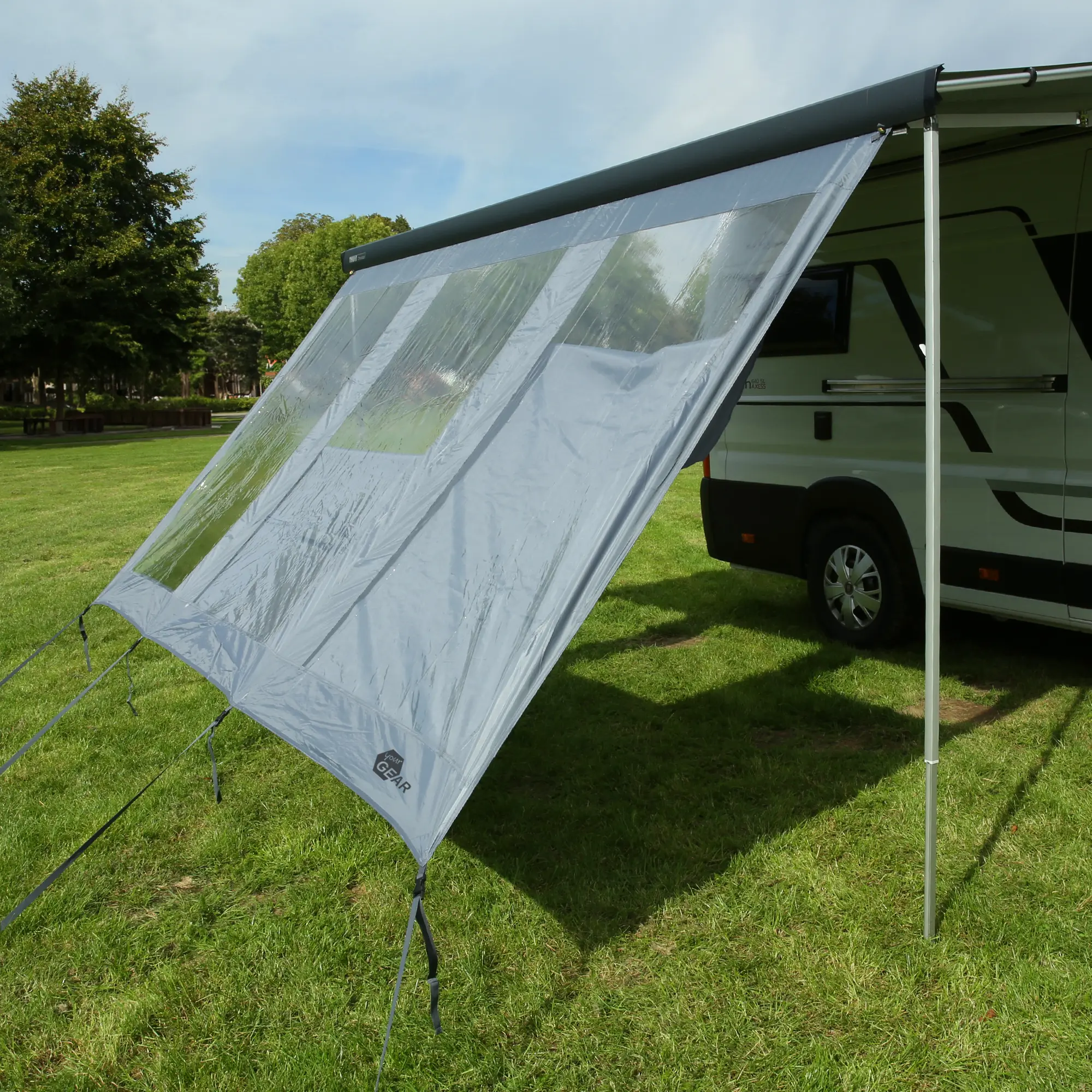 your GEAR Panorama Wall 2,8 x 2 m als transparente Markisenwand am Wohnmobil montiert, schützt vor Sonne, Wind und Regen, mit großen Sichtfenstern und Abspannleinen auf grüner Wiese.