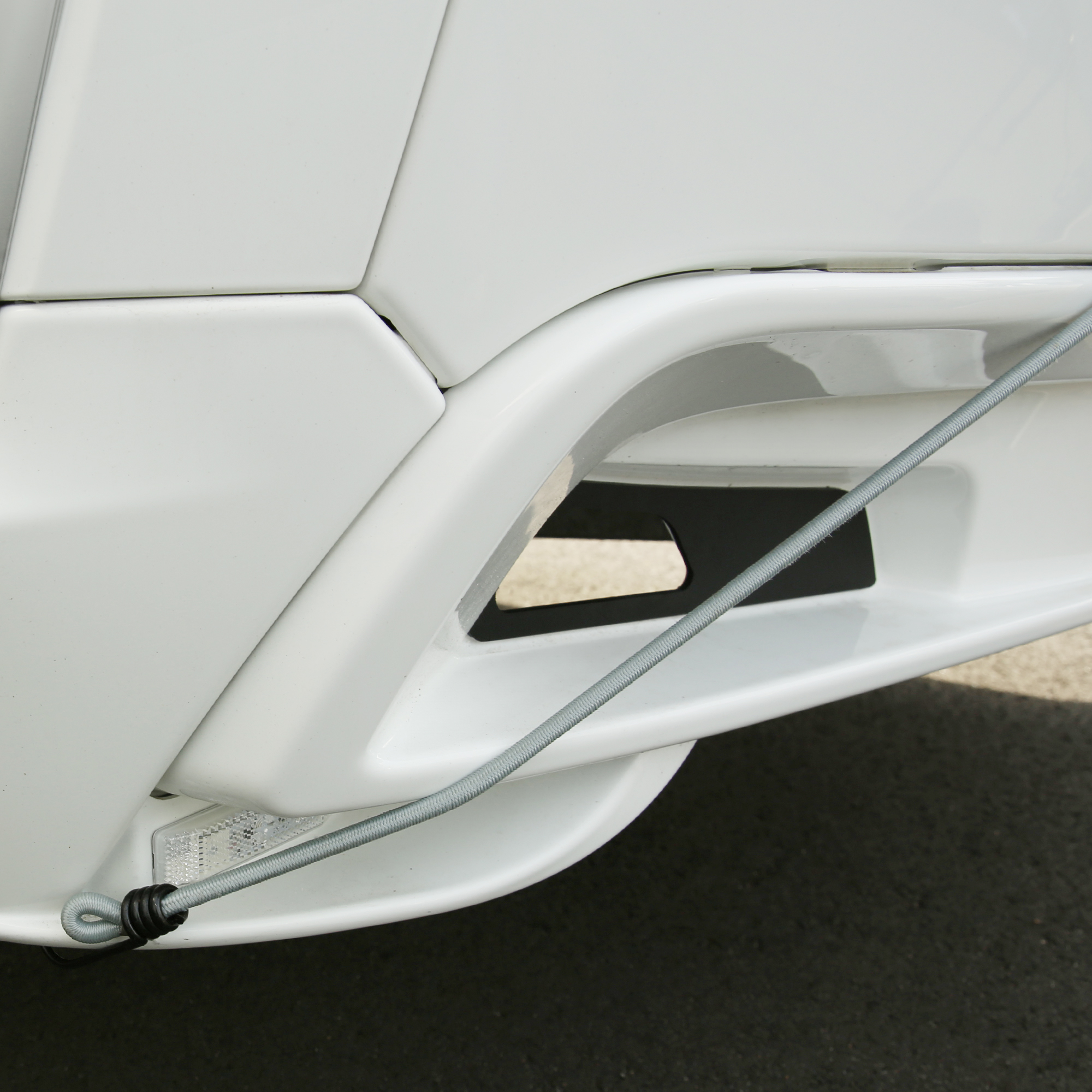 Close-up of your GEAR caravan thermo bug protection cover, showing the elastic cord securely fastened to the front or rear of a white caravan. Designed for all-season protection, measuring 200 x 160 cm.