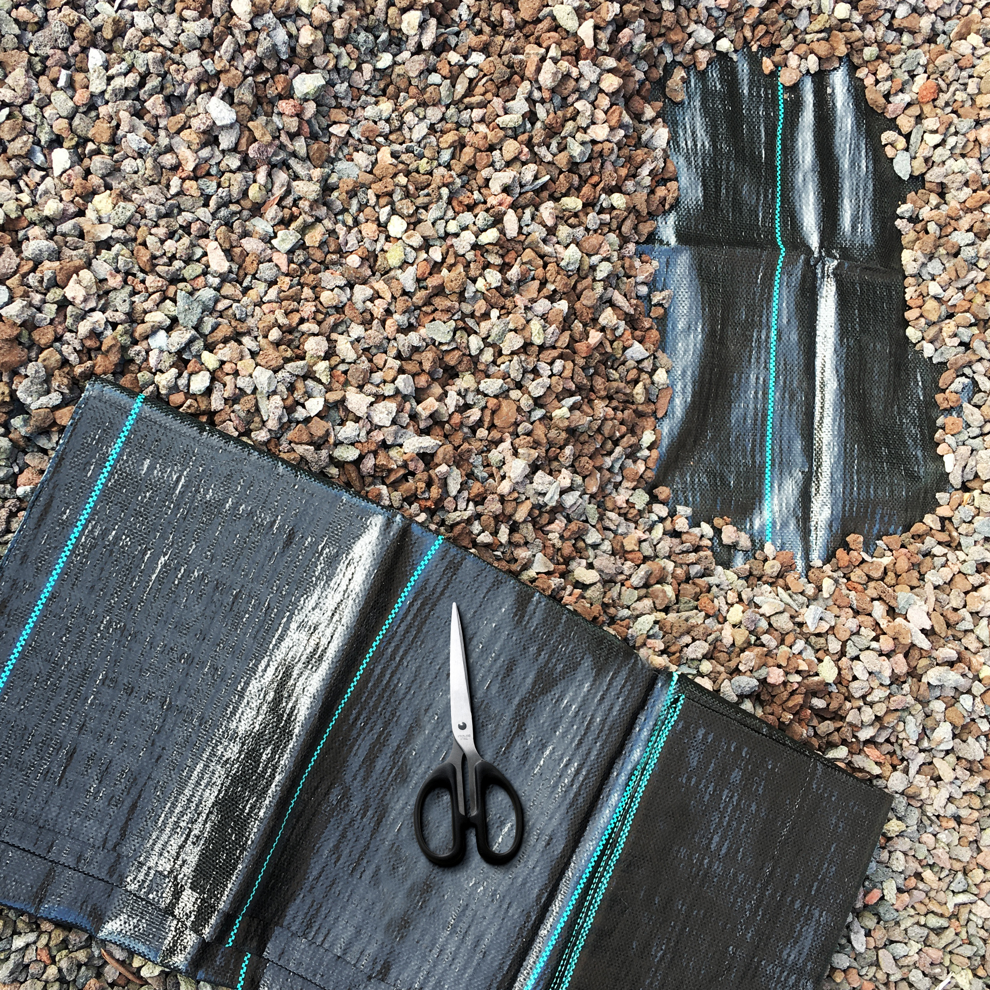 yourGEAR weed control fabric 10 m², black woven garden fleece with blue lines, shown on gravel with scissors for cutting, demonstrates tear-resistant, water-permeable, UV-stable weed barrier.