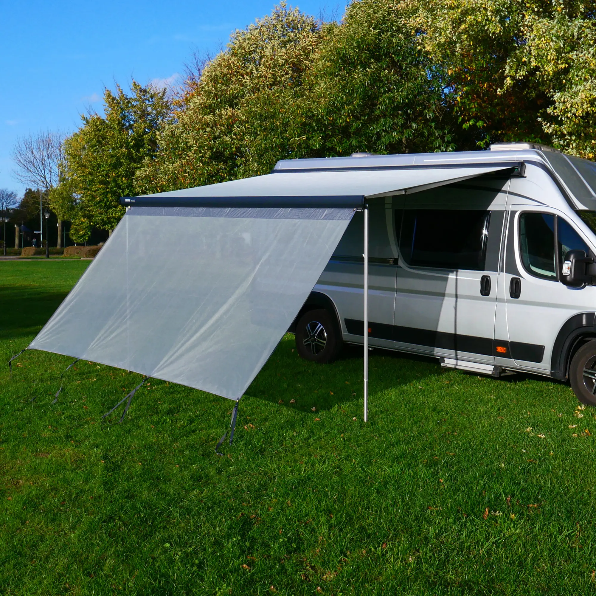 Vorderwand your GEAR Capri Sun Blocker 2,8 x 2 m, montiert an Campingbus-Markise, lichtdurchlässiges Spezialgewebe als Sonnen- und Sichtschutz, gespannt mit Abspannleinen auf grüner Wiese.