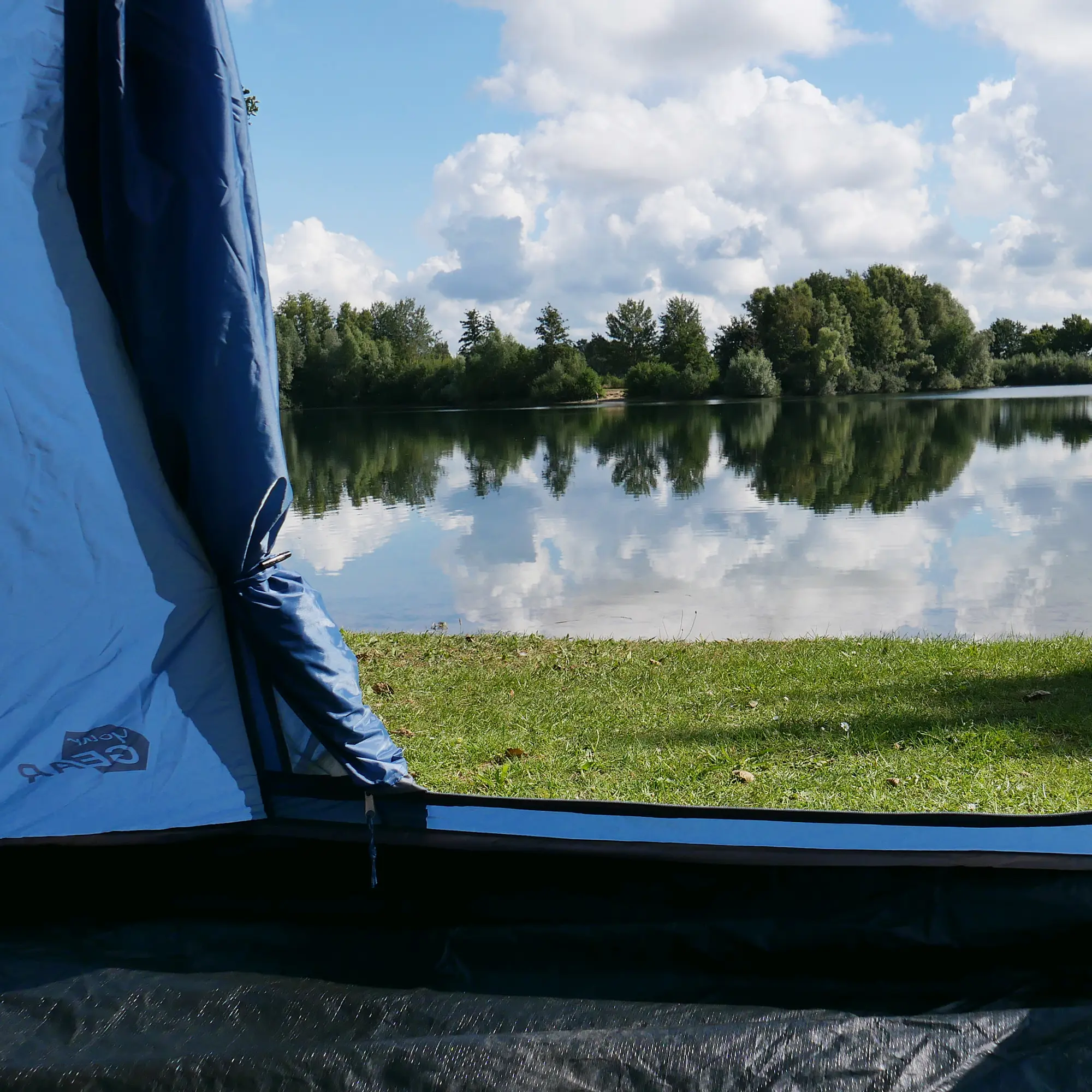 your GEAR Lido 290 tipi tent for 3 people, shown with waterproof 5000 mm sewn-in bathtub floor and insect protection, set up by a lake with open entrance and logo visible on light blue fabric.