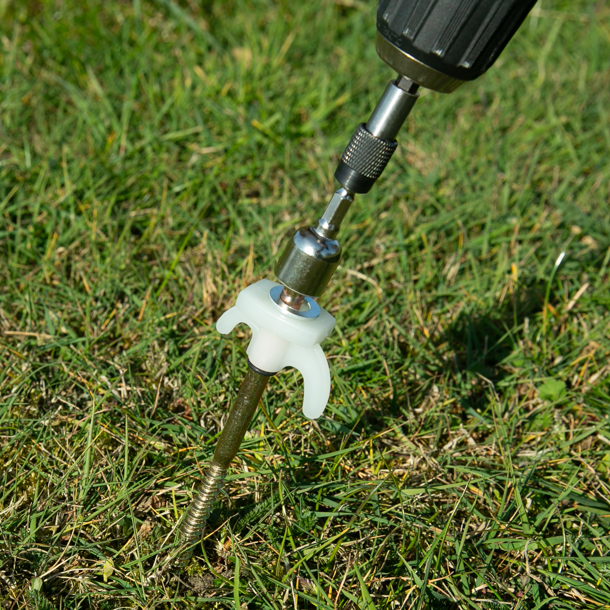 Robuster your GEAR Schraubhering aus Stahl mit fluoreszierendem Kunststoffkopf, Sechskantkopf und Gewinde, eingesetzt mit Akkuschrauber im Gras – ideal für Zelt, Camping und harten Boden.