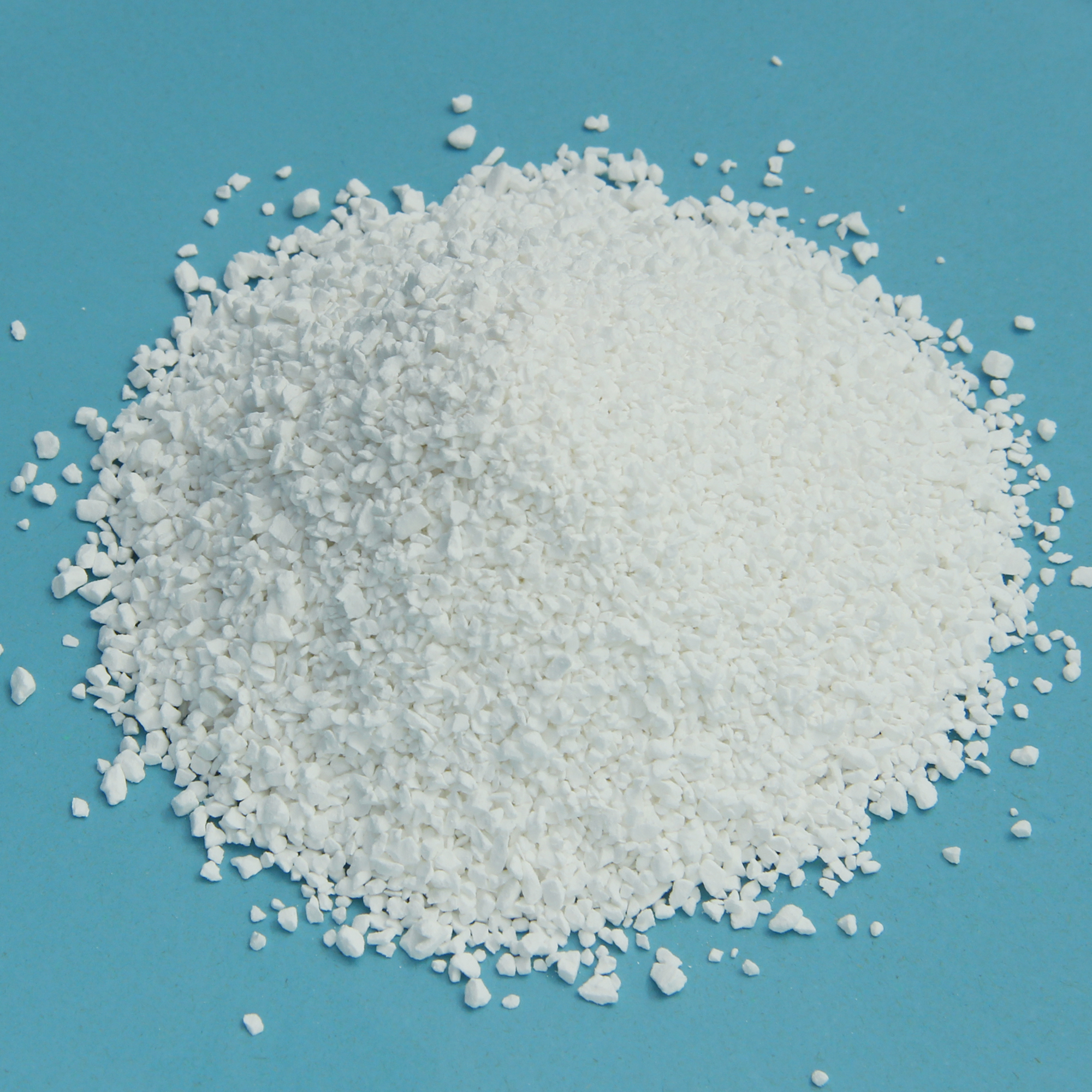 Chlorgranulat yourGEAR 1 kg, schnelllöslich, weißes Granulat mit 56% Aktiv-Chlor zur Pooldesinfektion gegen Algen, Bakterien, Pilze und Viren, auf blauem Untergrund.