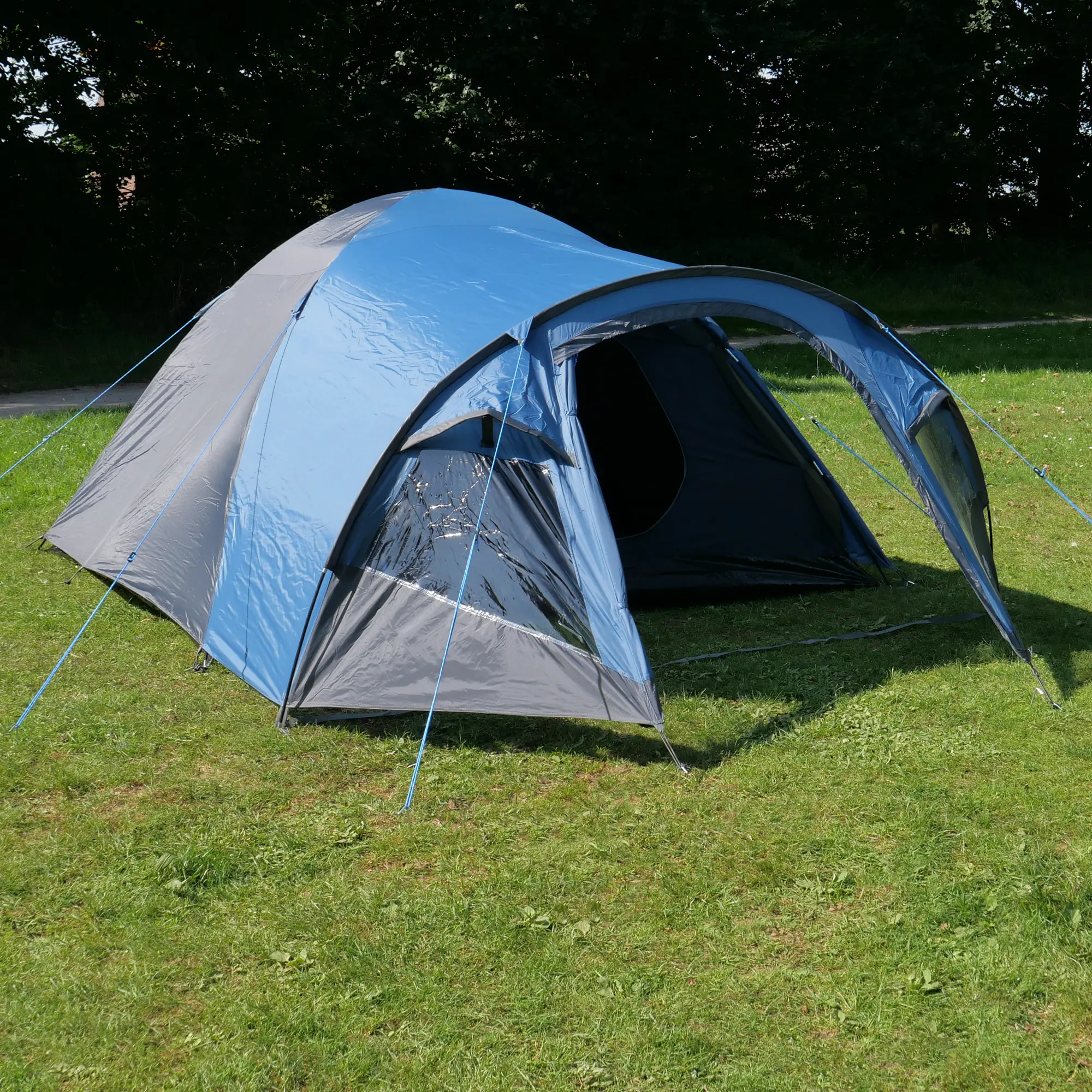 yourGEAR Posada 4 dome tent in blue-grey for 4 people, with large vestibule, side window, two entrances, ventilation openings, and waterproof flysheet, set up on grass with guy lines visible.