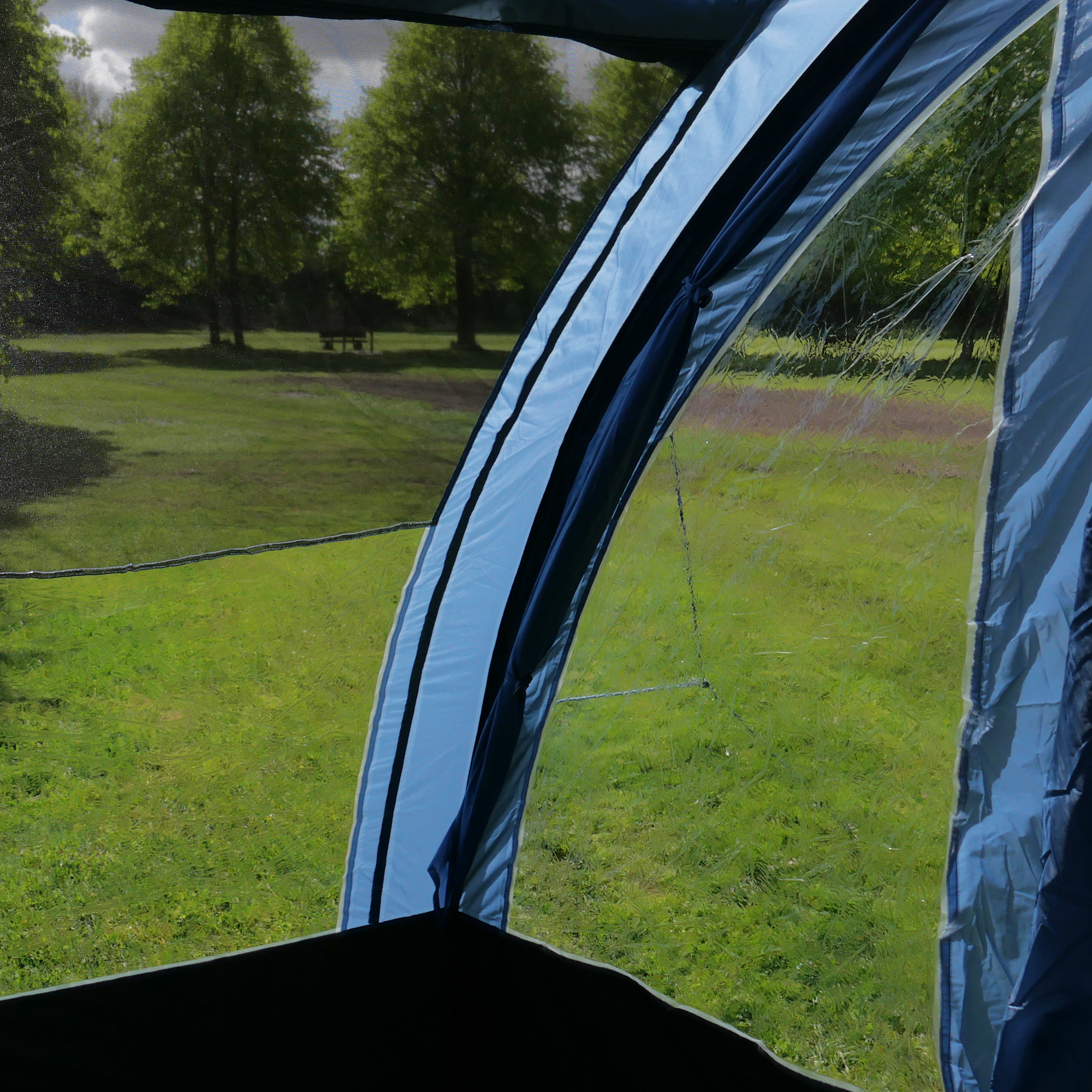 Vue intérieure du your GEAR Zelt Mistral, tente tunnel familiale 6 personnes, grandes fenêtres latérales en polyglas et mesh assurant lumière et aération, structure bleue, vue sur un espace vert à l’extérieur.