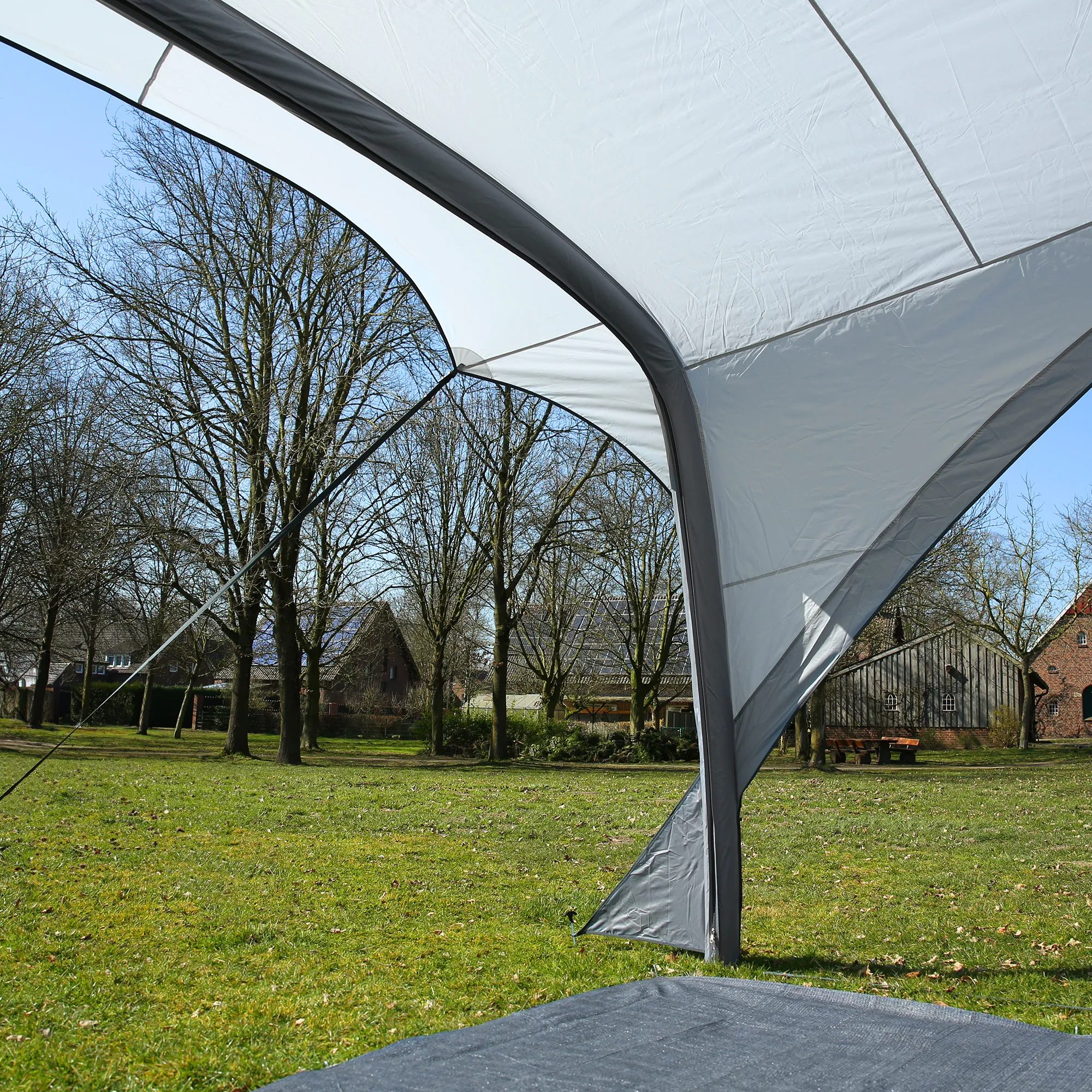 Auvent gonflable your GEAR Caravan Amalfi Air 3.6 gris clair avec boudins d'air sombres, tissu UV50+ tendu, haubans et piquets ancrés sur pelouse, vue rapprochée de la voûte et de la jonction au sol.