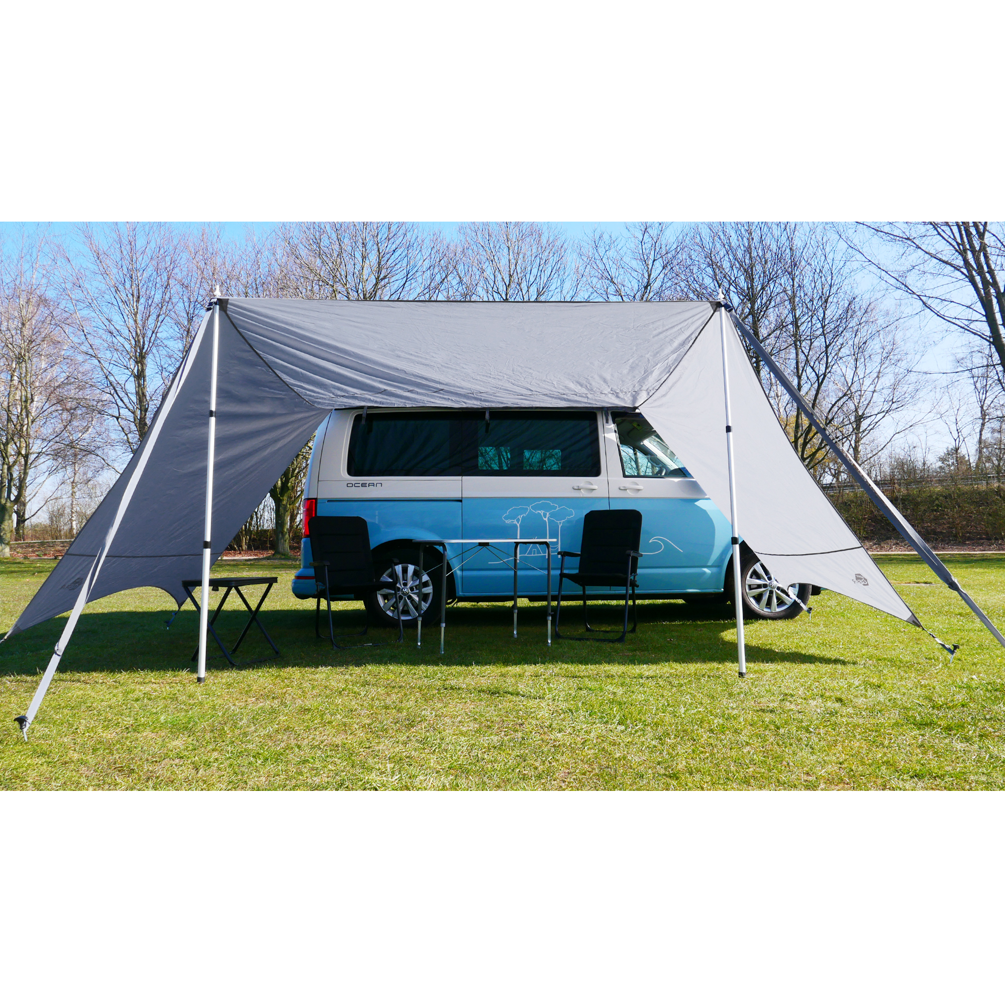 your GEAR Tropea Bus awning UV 50+ in gray with two side walls, set up beside a camper van, providing sun and rain protection; includes aluminum poles, outdoor chairs, and table underneath.