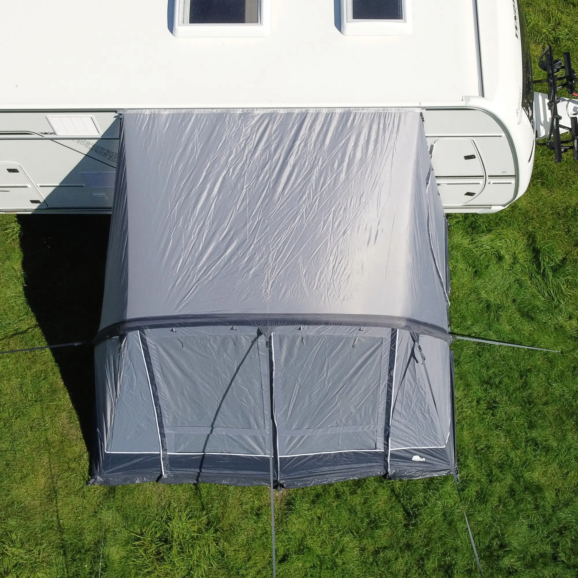 your GEAR Vicenza 350E AIR inflatable awning, attached to a caravan, grey color, 350x250 cm, single air tube system, triple keder, lightweight design, pitched on grass, top-down view.