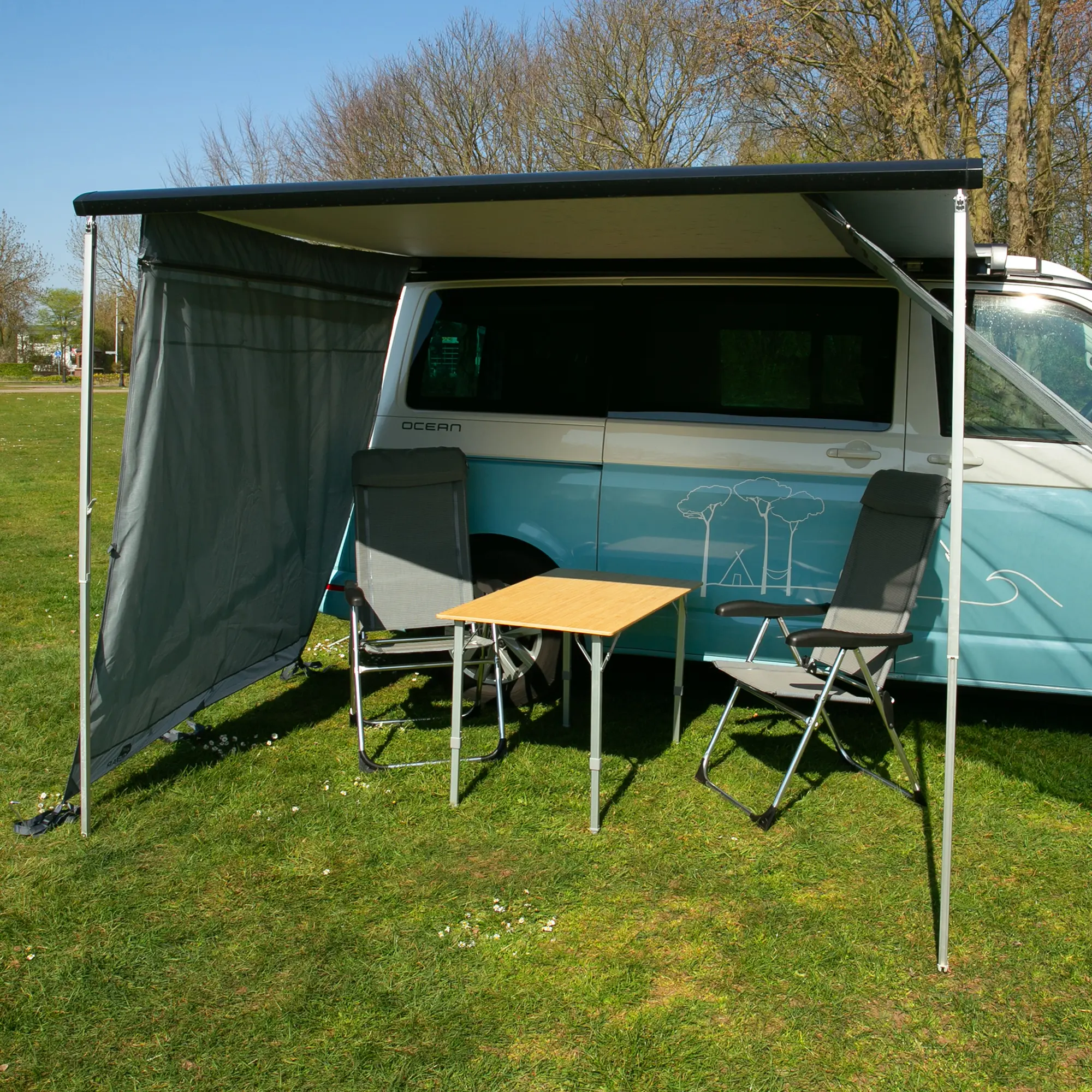 Paroi latérale your GEAR Sun + Rain Blocker montée sur une marquise de camping-car, protégeant du soleil et de la pluie, avec deux chaises et une table sous l’auvent. Idéal pour Thule, Fiamma, Dometic.
