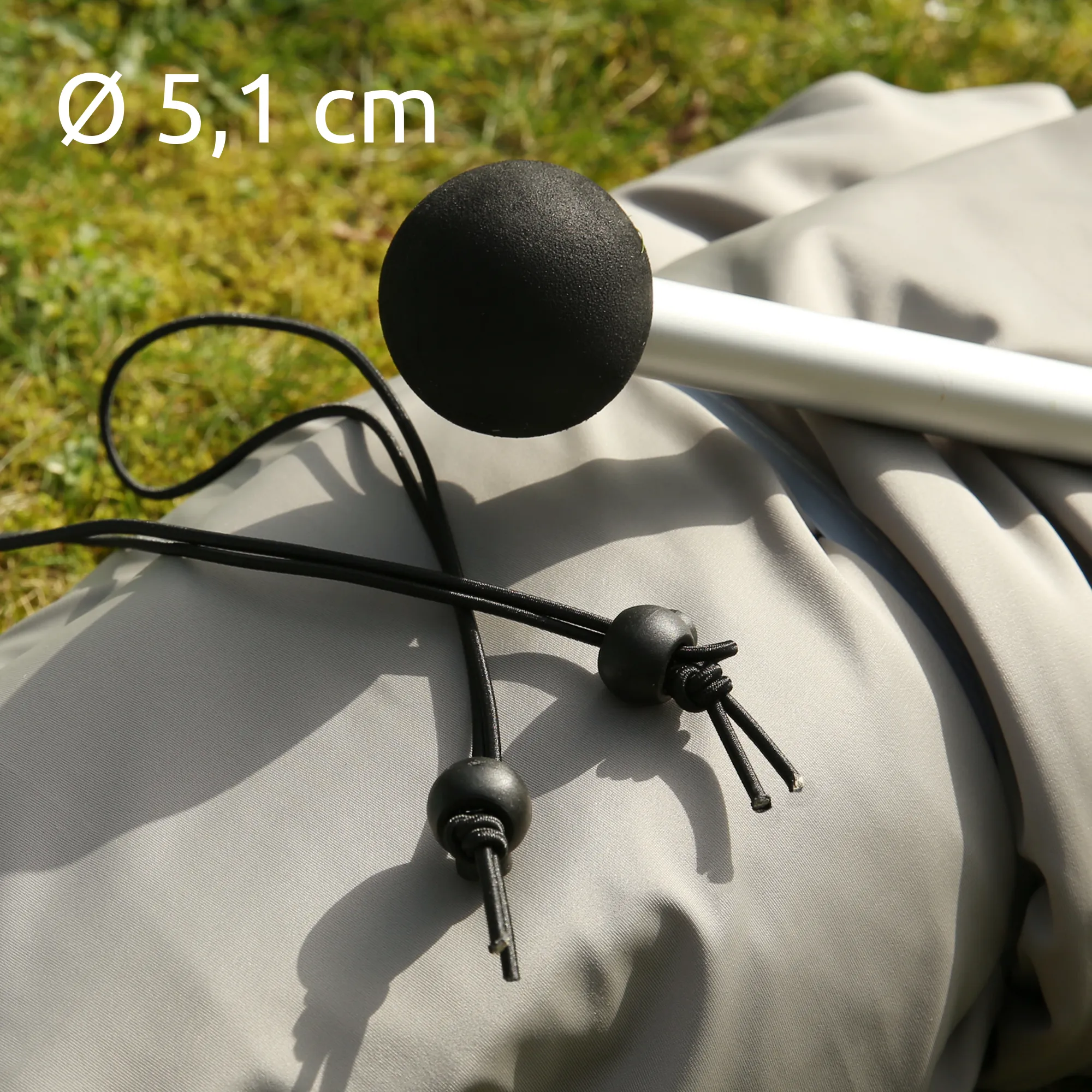 Détail de la Cameo Beach Shelter your GEAR : tissus Lycra gris clair posé sur l’herbe, hampe aluminium argentée avec embout noir sphérique, cordons élastiques noirs et stoppeurs ronds, diamètre indiqué Ø 5,1 cm.